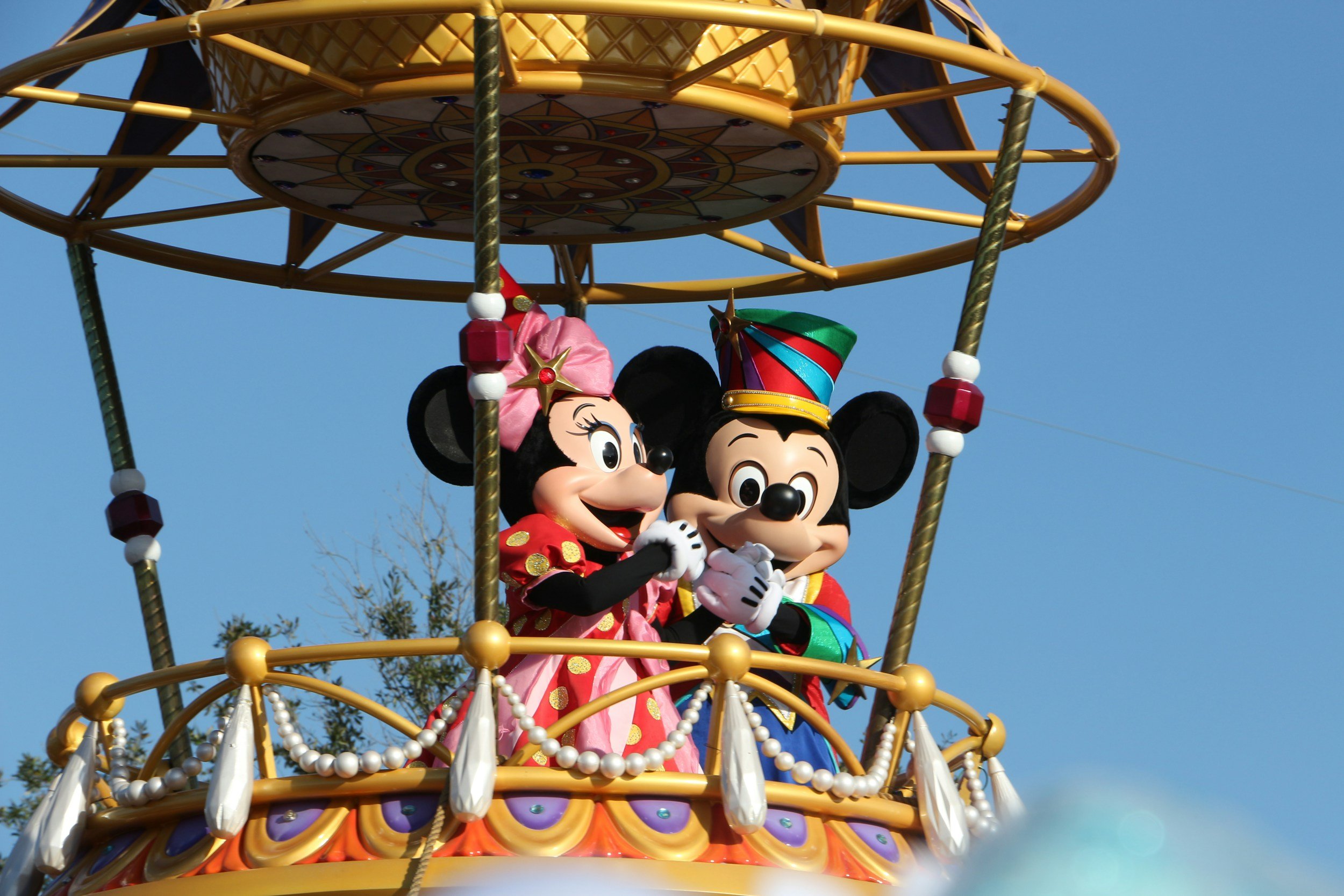 Minnie Mouse and Mickey Mouse in colorful costumes on a parade float with a blue sky background.