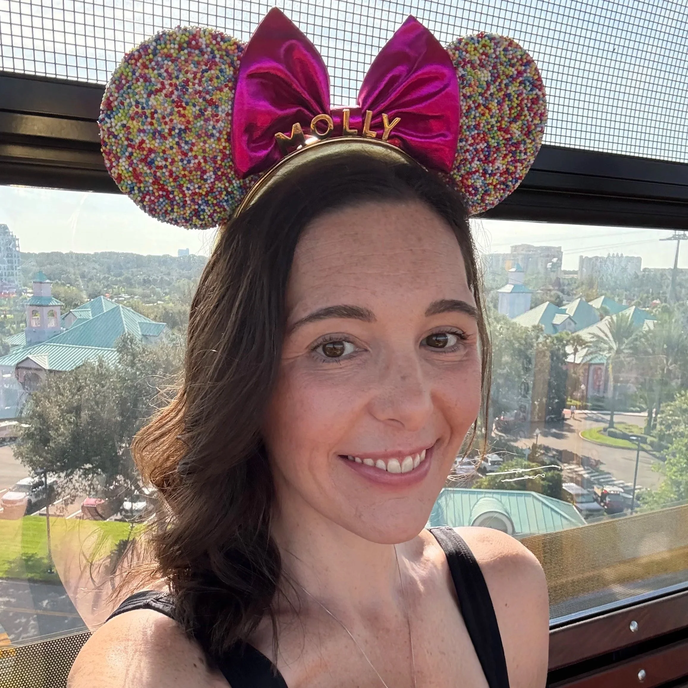Molly smiling at Walt Disney World wearing Minnie ears with a scenic park view in the background