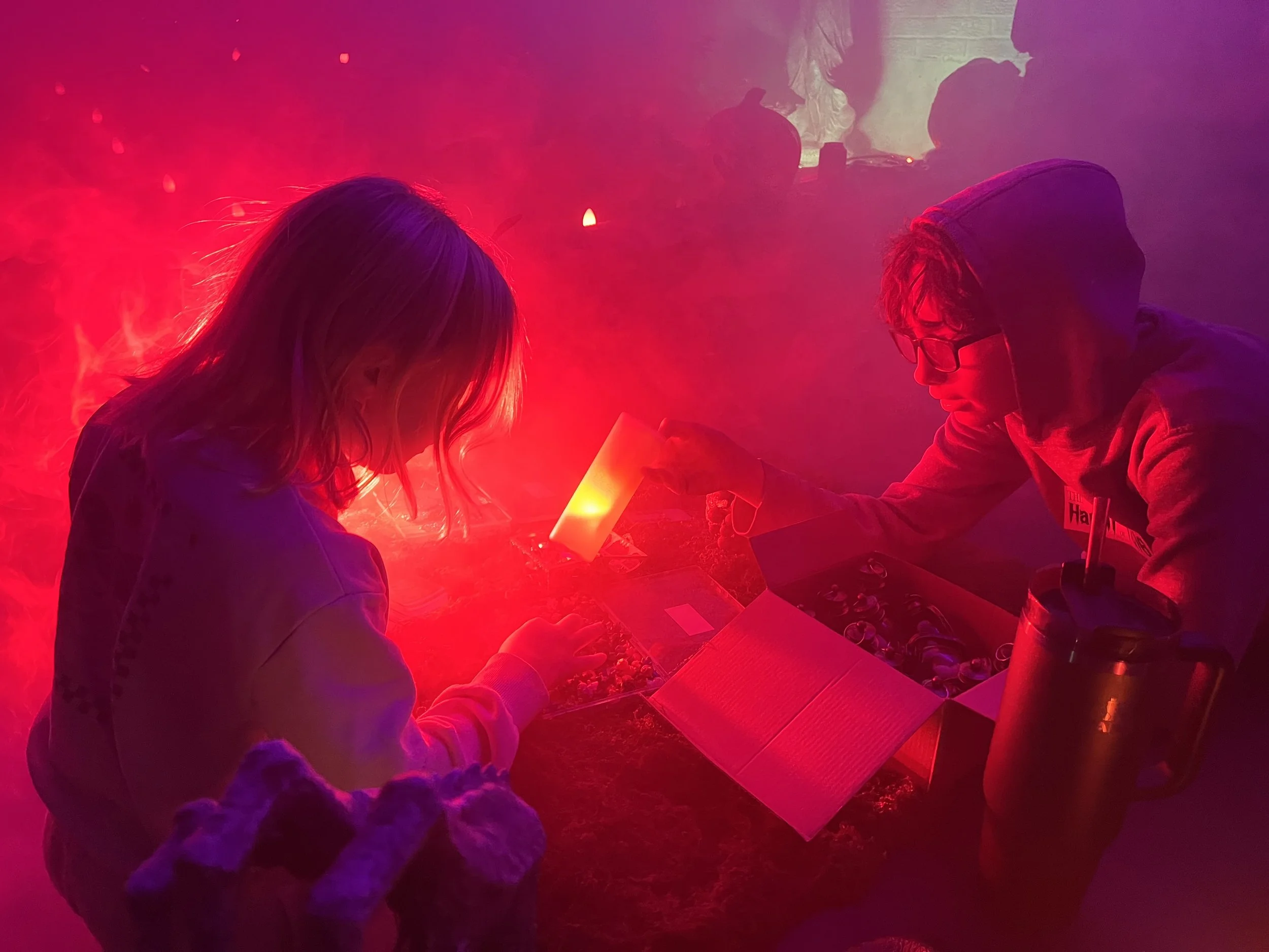 A small child illuminated with red atmospheric light chooses a tiny toy dragon from a plastic container