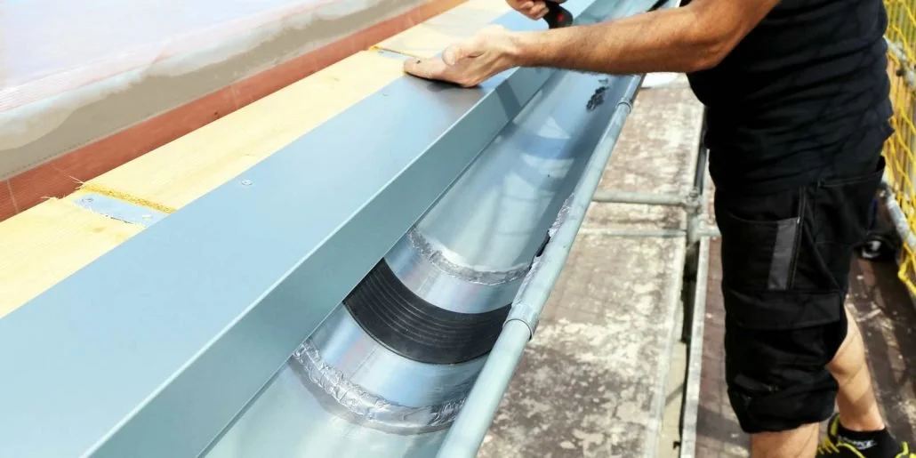 Persona che esegue lavori di installazione o manutenzione su una grondaia o condotto in metallo su un edificio, con scaffalature di sicurezza e strumenti di lavoro.