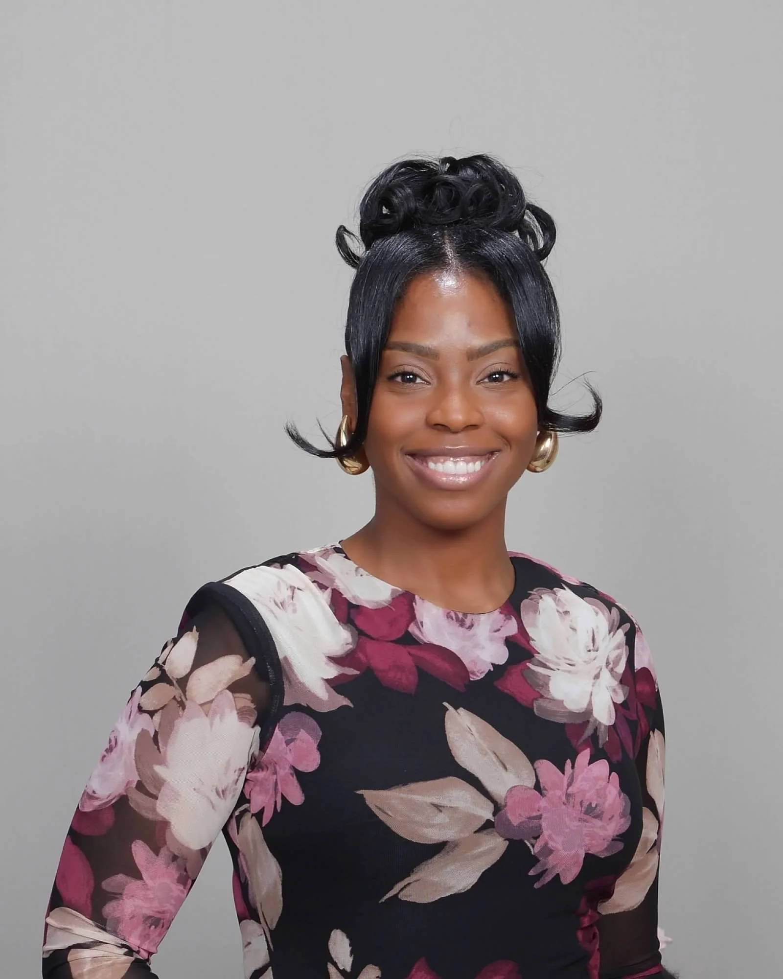 Smiling woman with black curly hair in a black turtleneck, wearing a necklace with a cross.