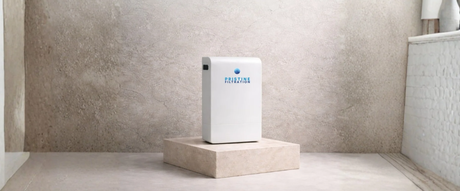 A white rectangular Pristine Filtration machine with a blue logo, placed on a beige pedestal against a textured beige wall.