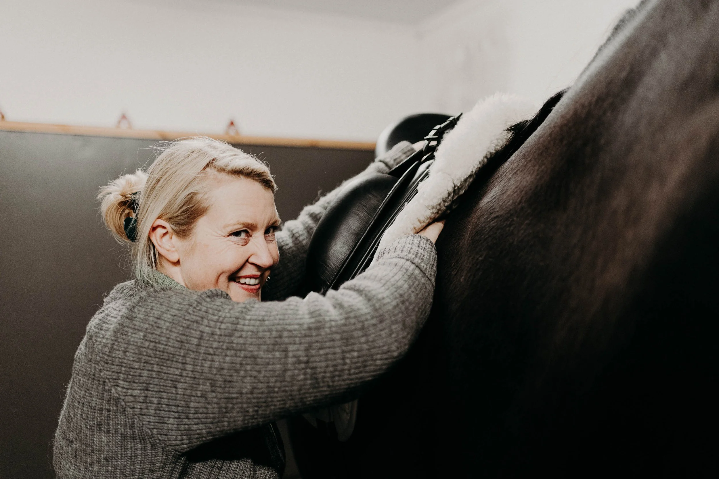 En smilende eldre kvinne som tilpasser en sal på en dressurhest.