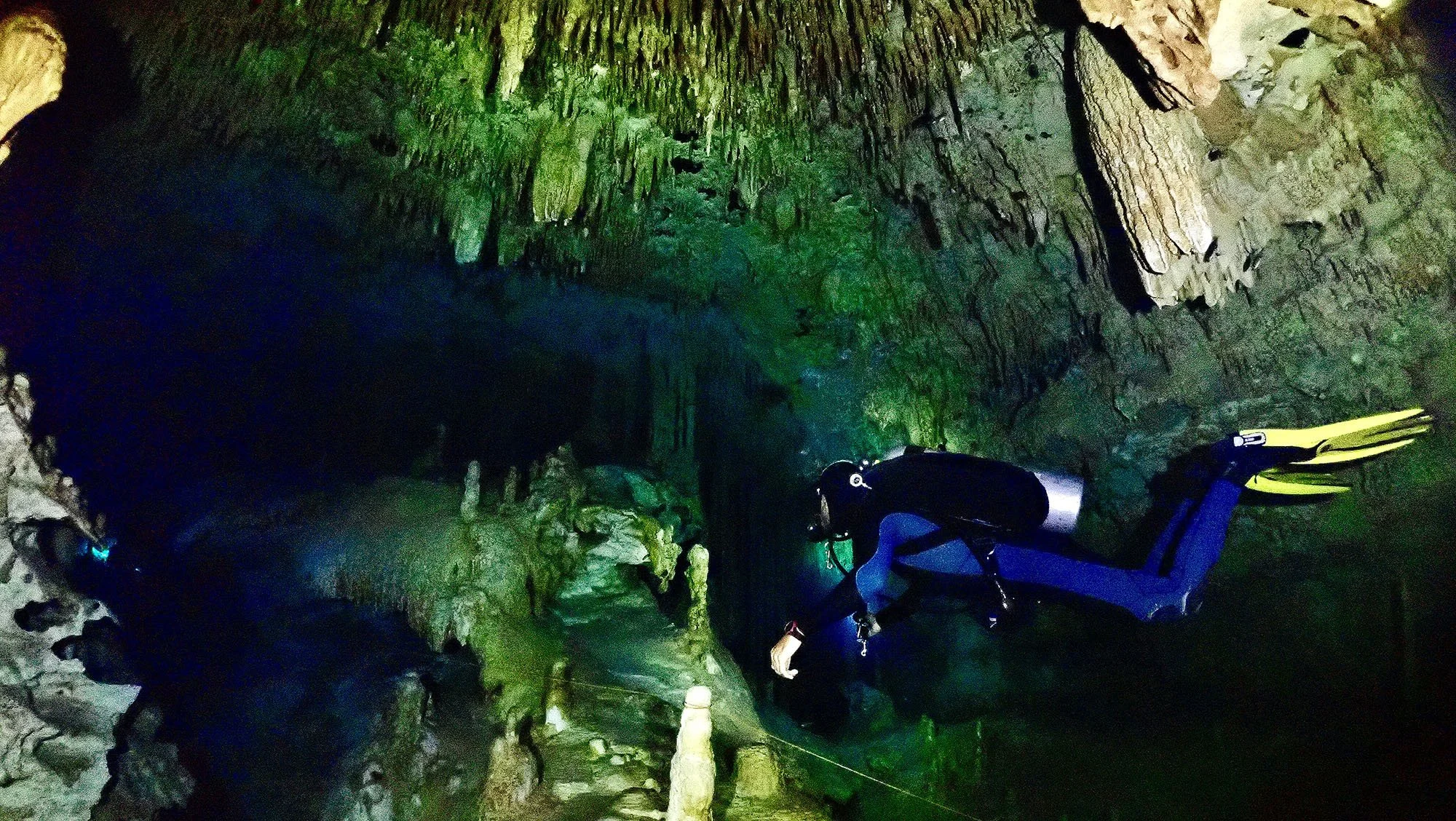 Scuba diver exploring an underwater cave with stalactites and stalagmites.