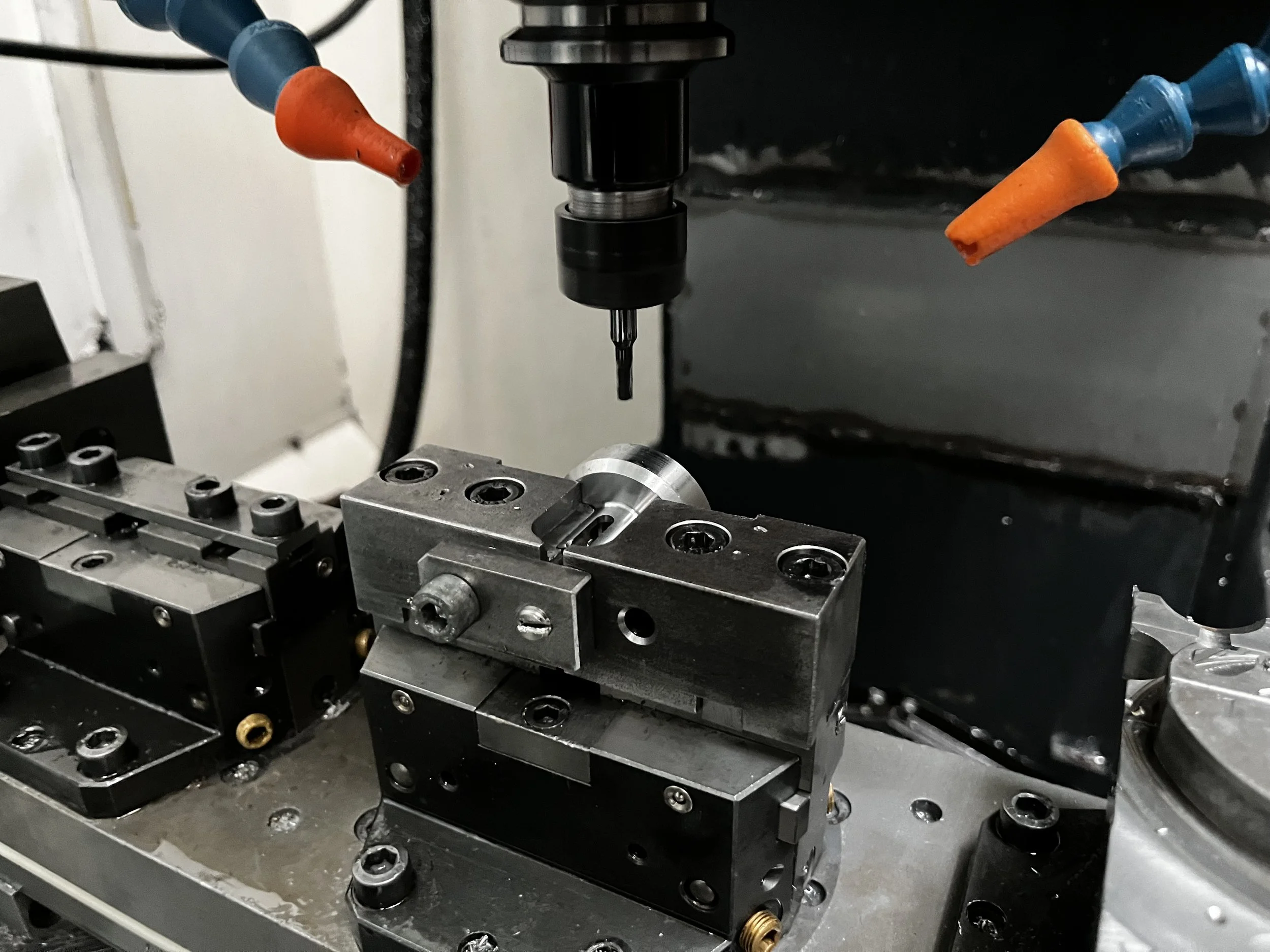 Nahaufnahme eines Werkzeugmaschinen-Teils mit Bohrfräser, die auf einer Metallvorrichtung befestigt ist, in einem industriellen Umfeld.