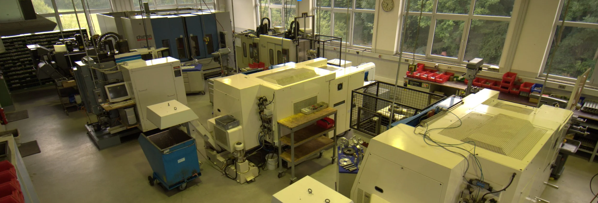 Einblick in eine Technikwerkstatt mit verschiedenen elektronischen Maschinen und Werkbänken, große Fensterflächen lassen Tageslicht herein.