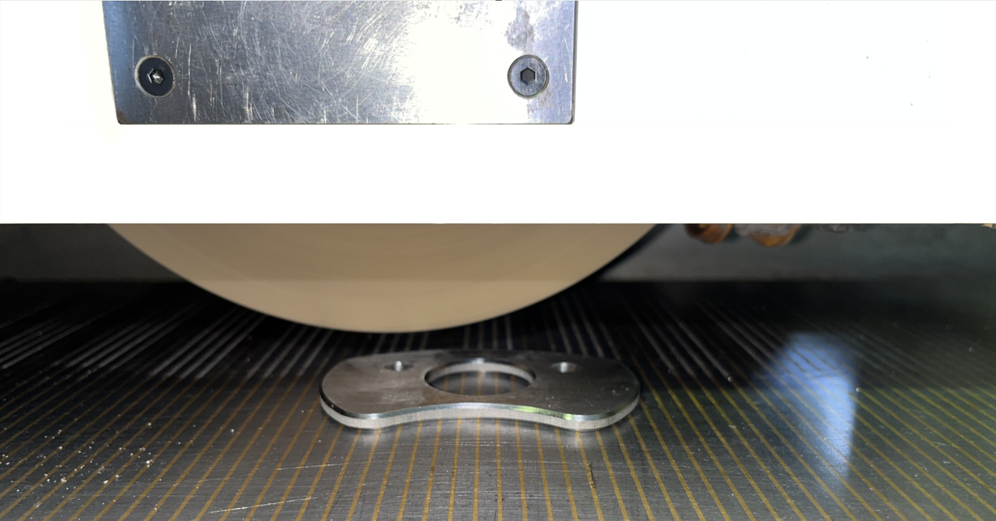 Metallteil mit vier Löchern auf einer schwarzen Oberfläche, Teil einer Maschine, oben eine Metallplatte mit Schrauben