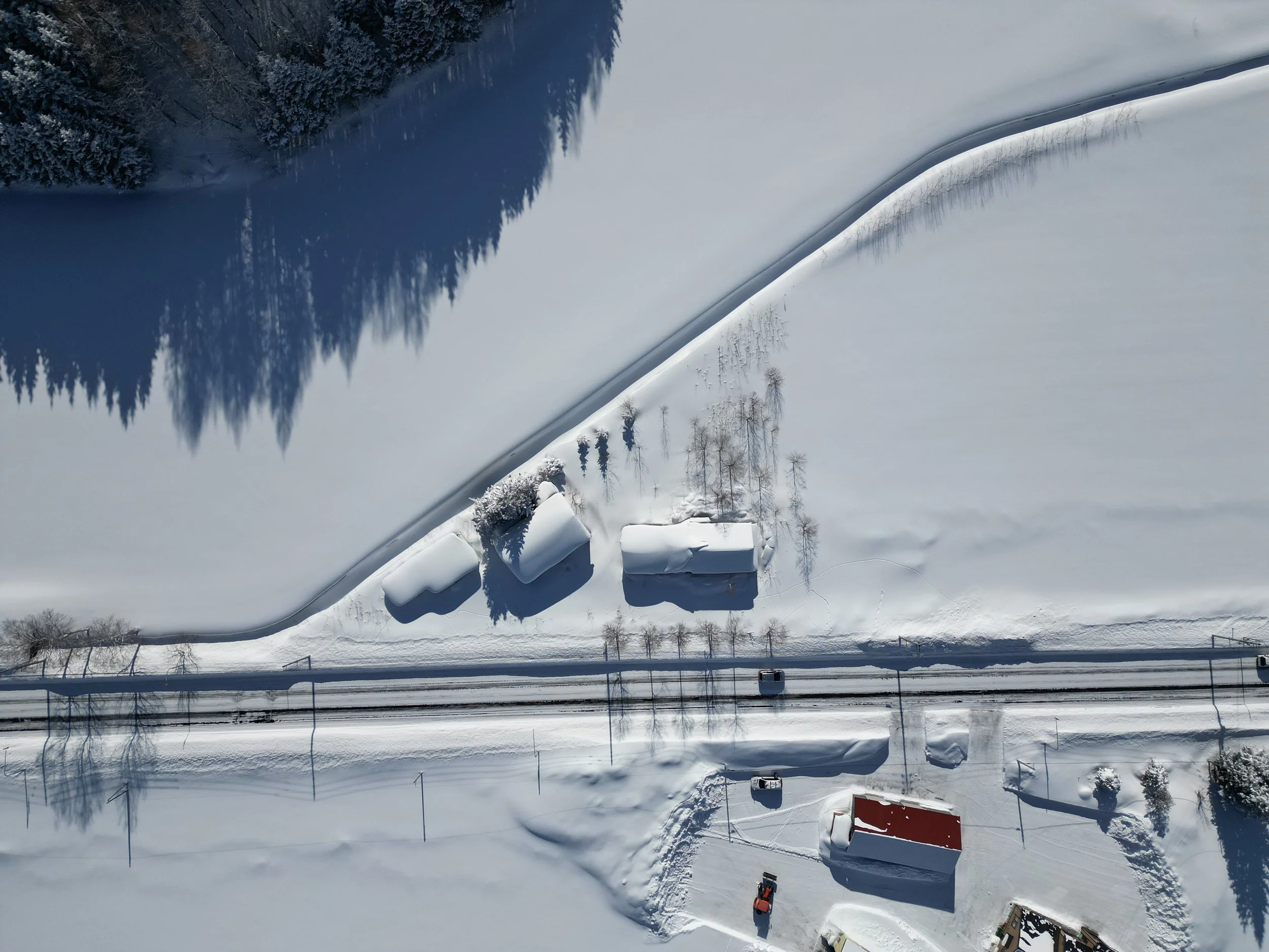 Aerial view of snow-covered landscape with trees, buildings, and road