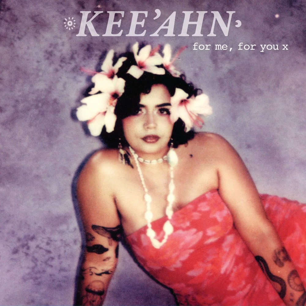 A woman with dark hair wearing a flower crown, a red strapless dress, and jewelry, posing against a purple textured background.
