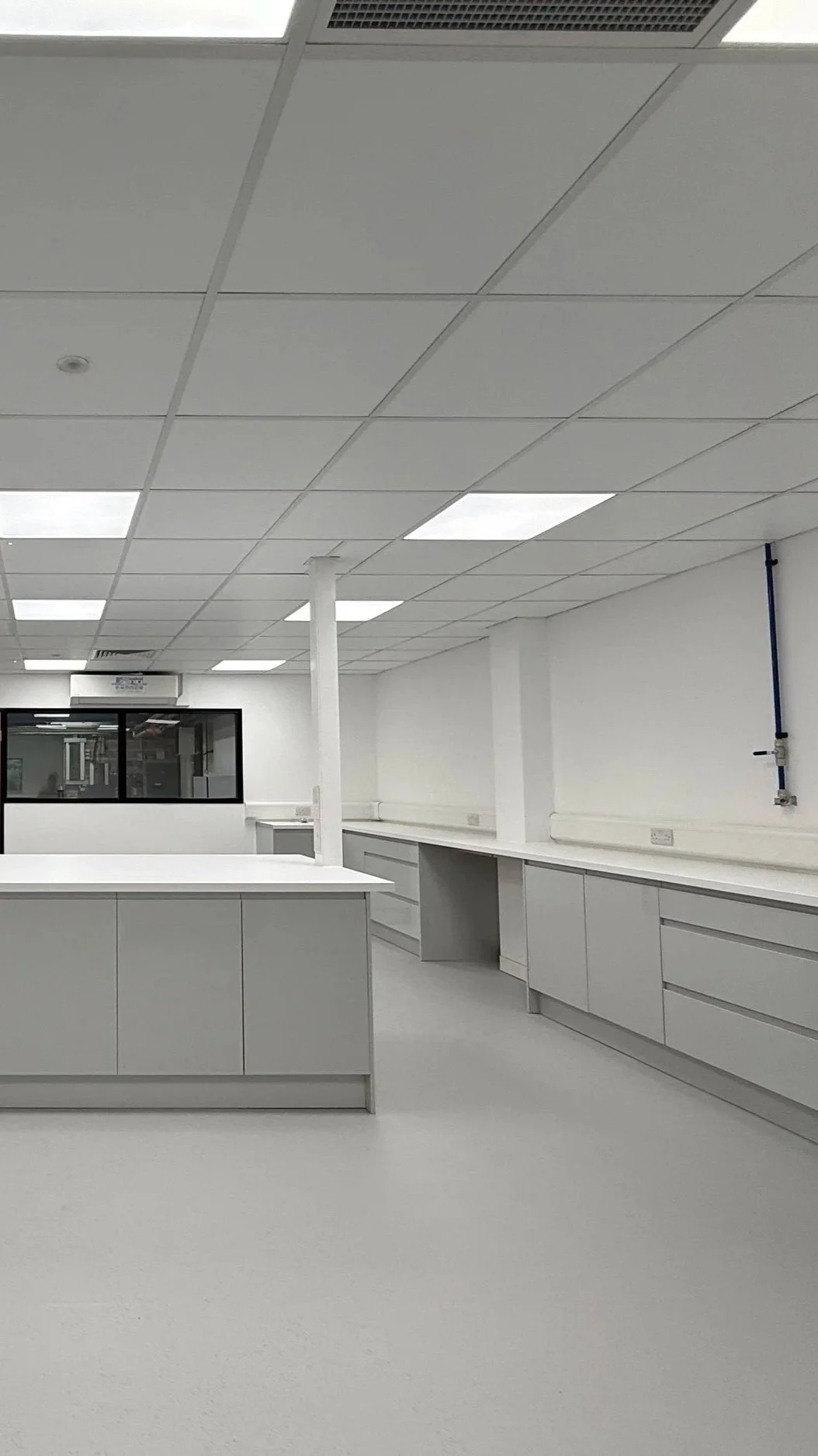 Empty laboratory or clean room with white cabinets, ceiling tiles, and fluorescent lights.