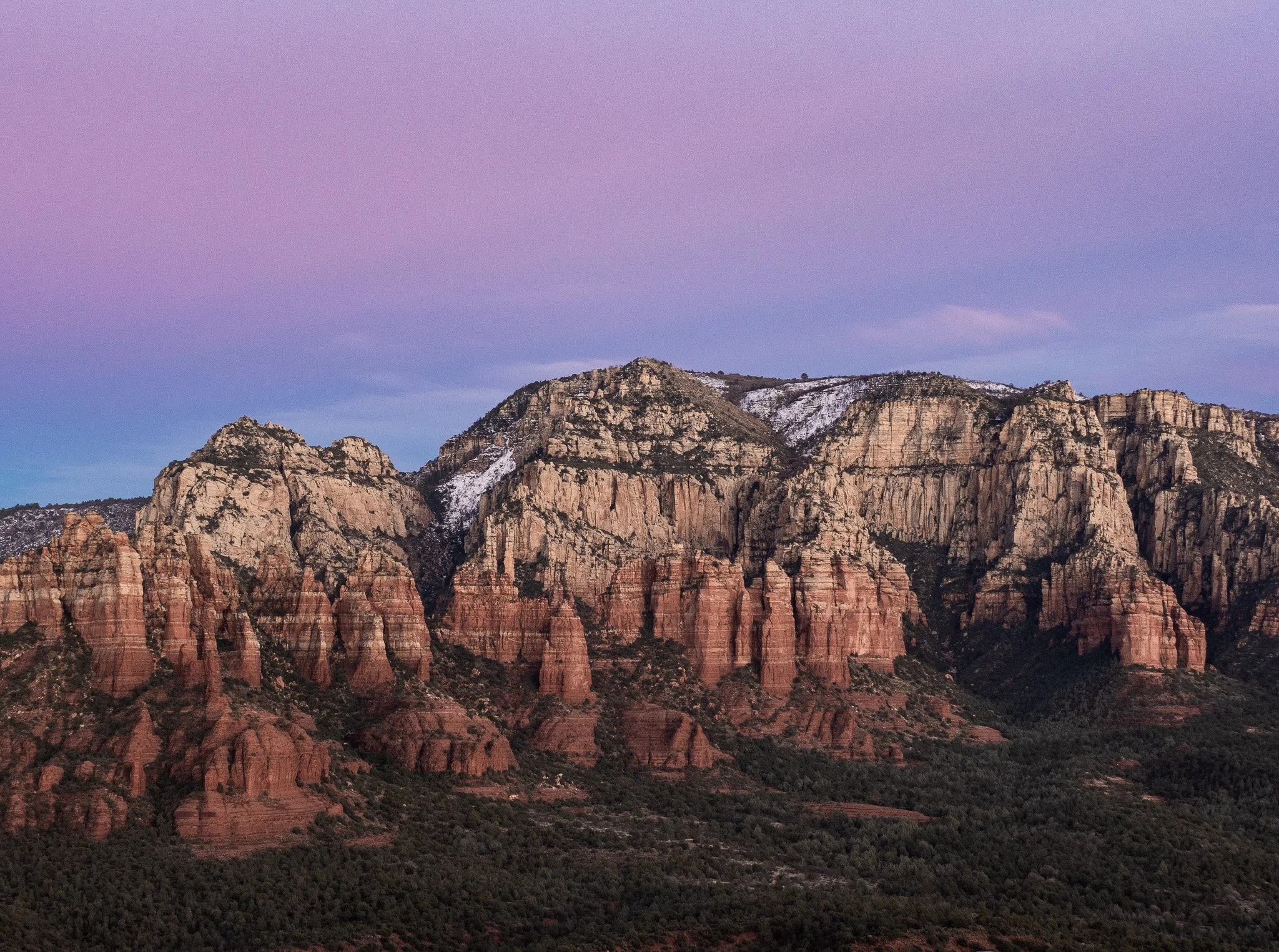 Sedona red rock cliffs glowing under a soft pink and purple sky with snow patches on the high ledges.
