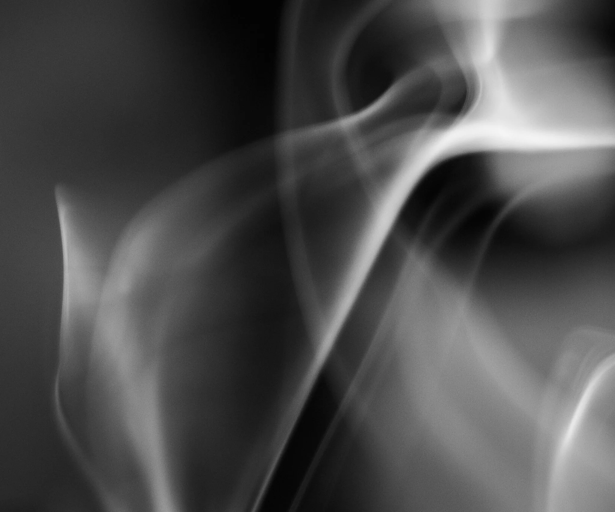Abstract black and white close-up photo showing delicate wisps of incense smoke curling against a dark background.