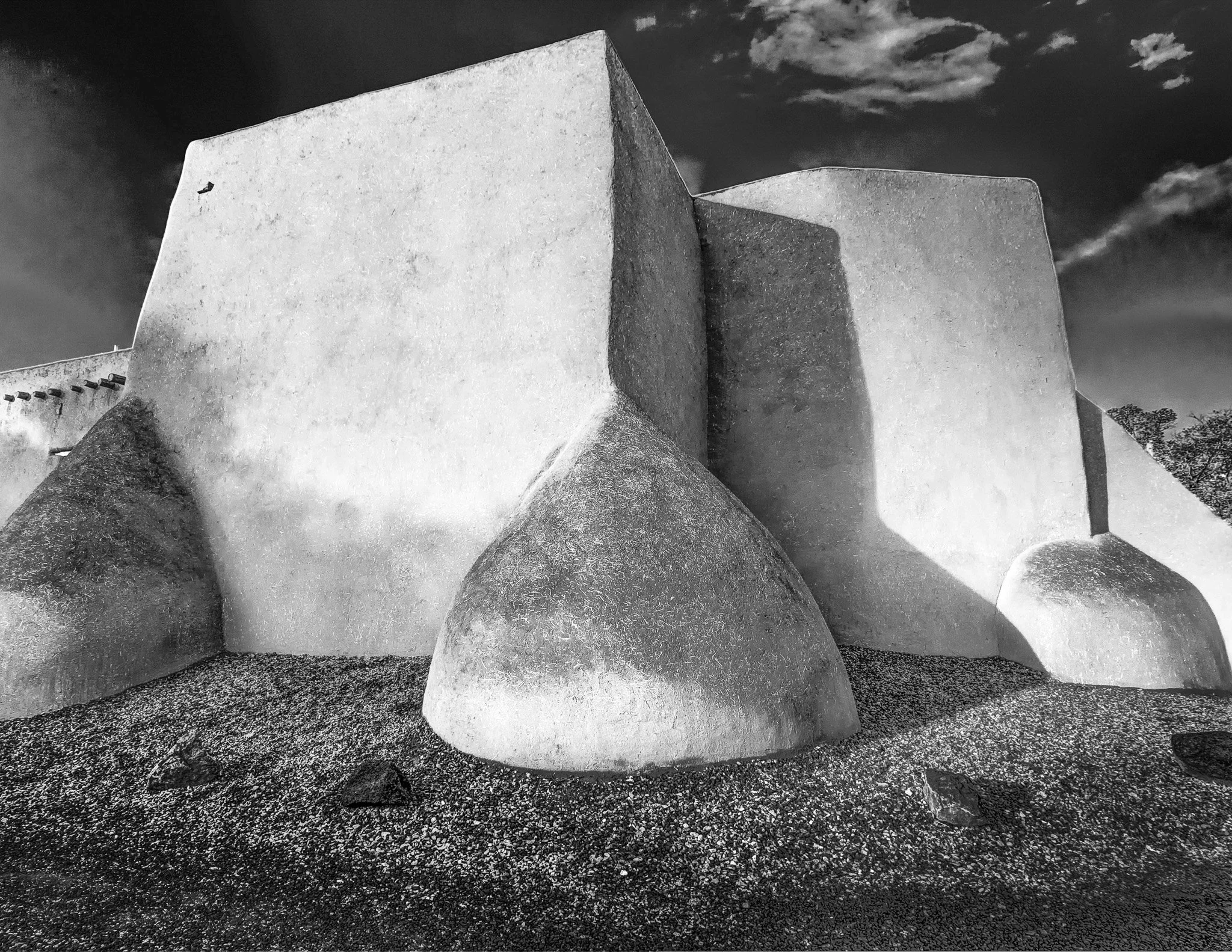 Black and white photo of the rear adobe buttresses of the historic San Francisco de Asis Church in Taos, New Mexico, highlighting dramatic shadows.