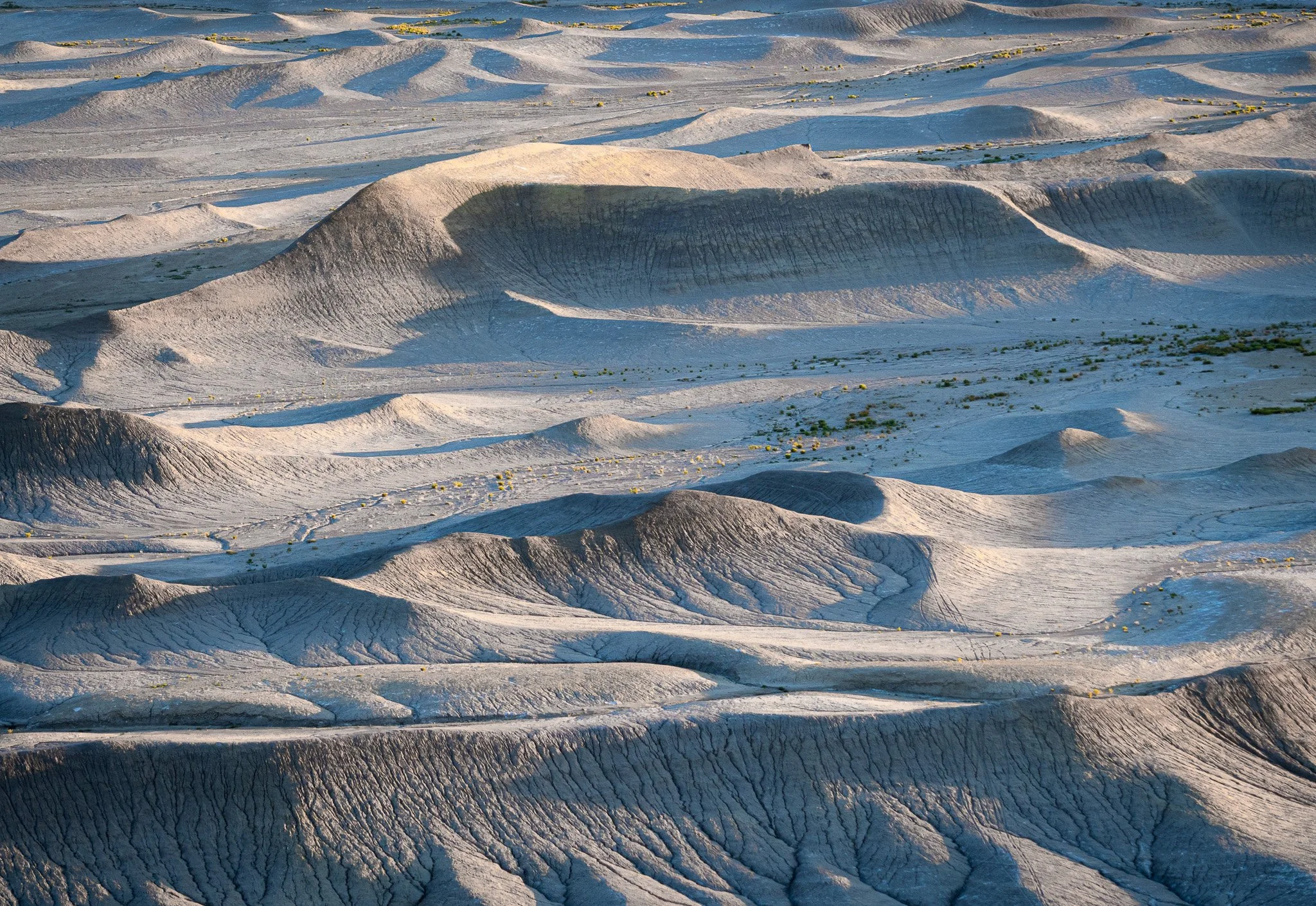 Aerial-style landscape of the gray, wind-sculpted clay hills at Moonscape Overlook in Utah under dramatic morning side-lighting.