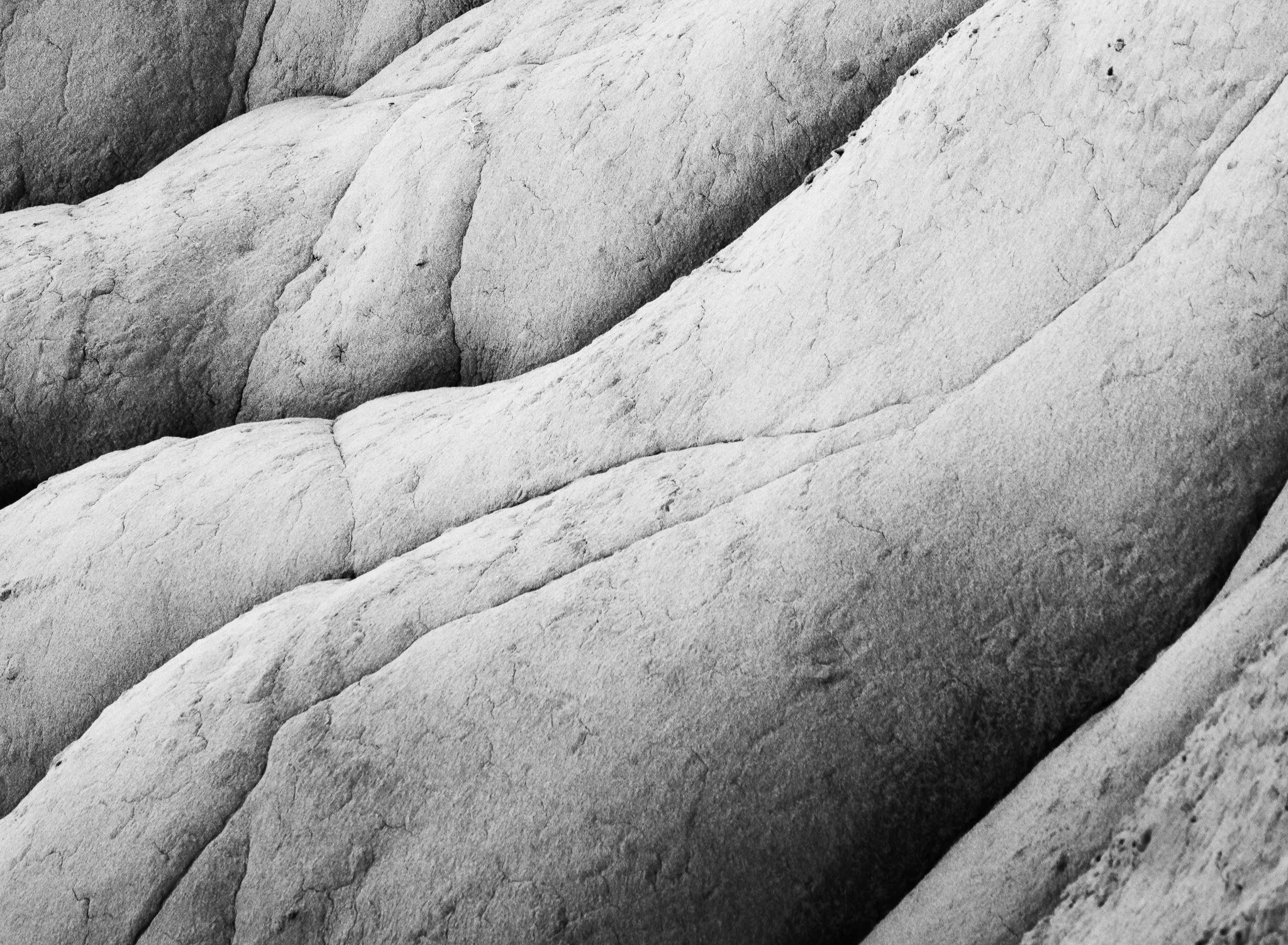 Black and white close-up of deeply eroded clay hills in New Mexico, showcasing flowing textures and shadows.