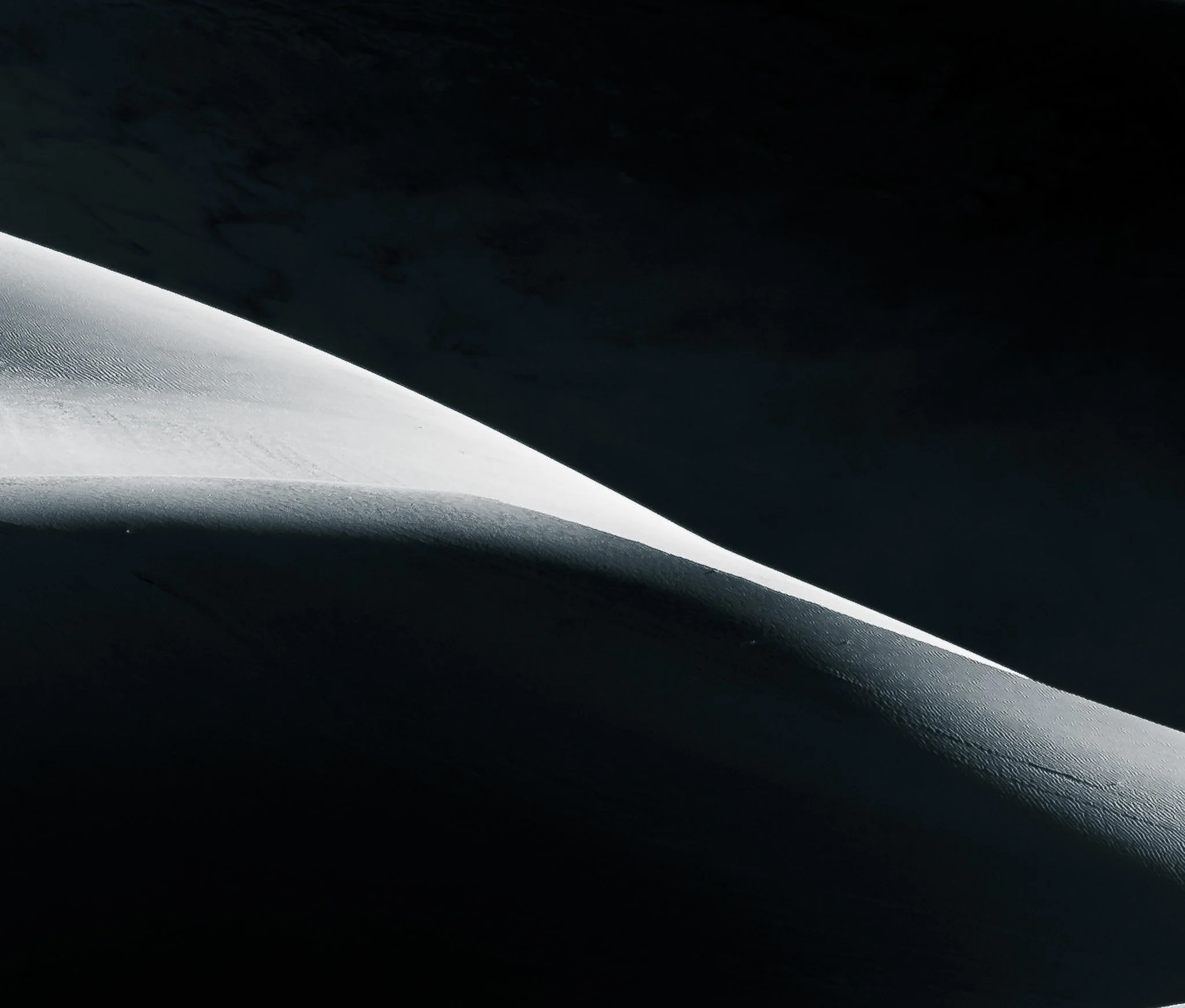 Black and white minimalist photograph of a glowing sand dune crest sweeping across dark desert shadows.