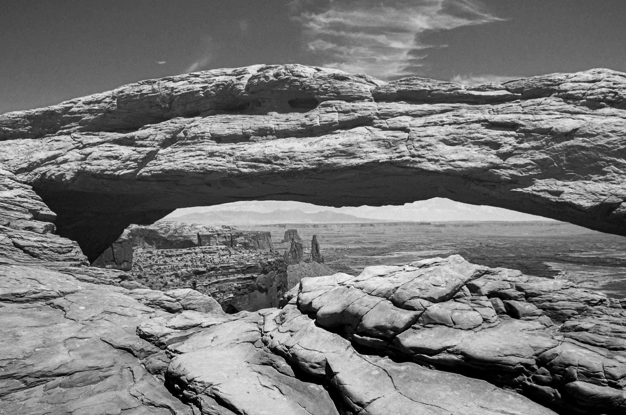 Black and white ultra-wide photograph of Mesa Arch framing the distant canyons and La Sal Mountains in Canyonlands National Park.