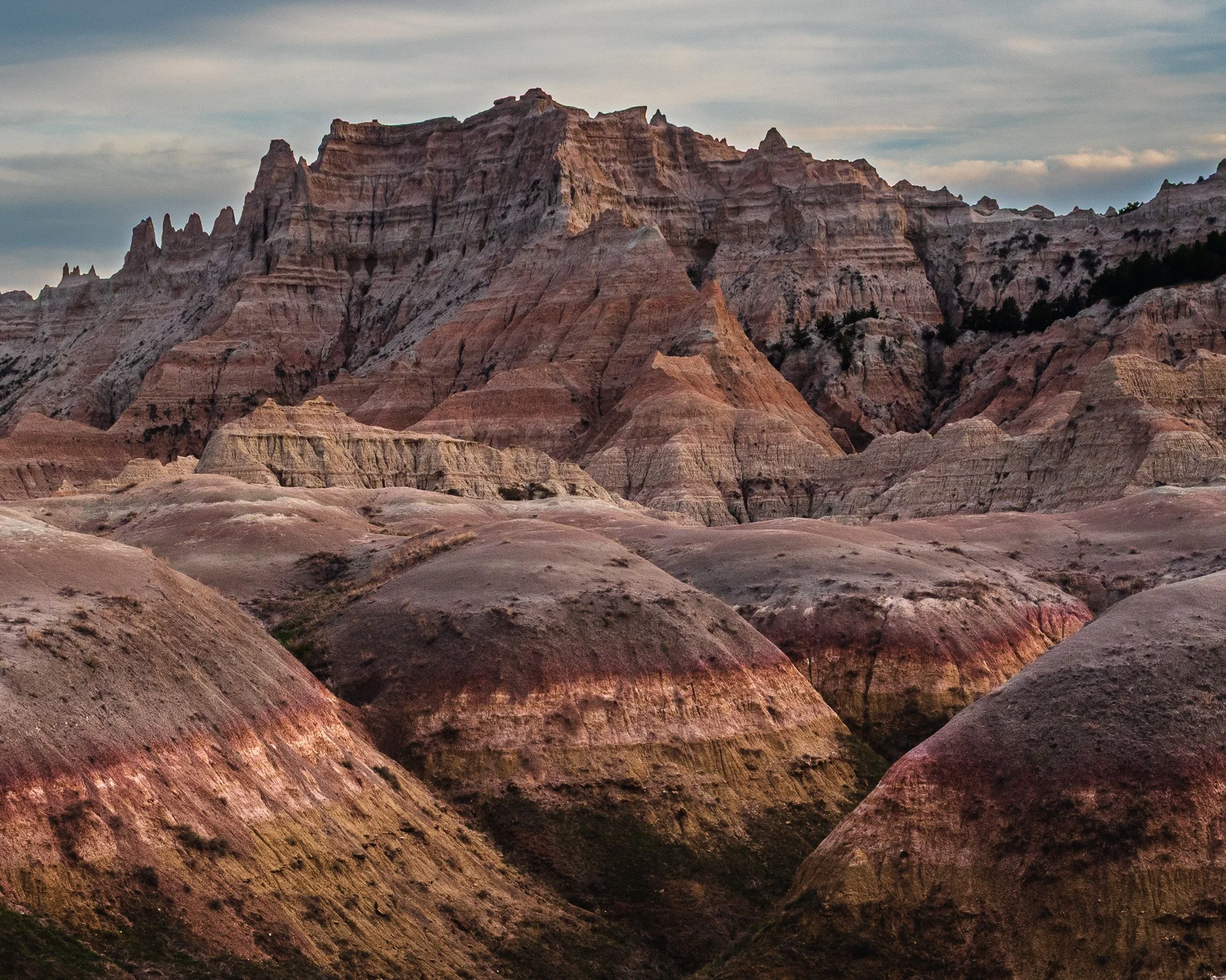 Layered colorful rock strata and smooth foreground mounds meet rugged spires under a soft sky in Badlands National Park.