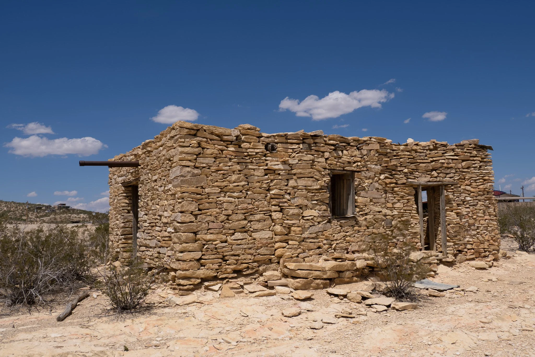 A well-preserved historic stone building made of flat stacked sandstone under a bright blue sky in Terlingua ghost town, Texas.