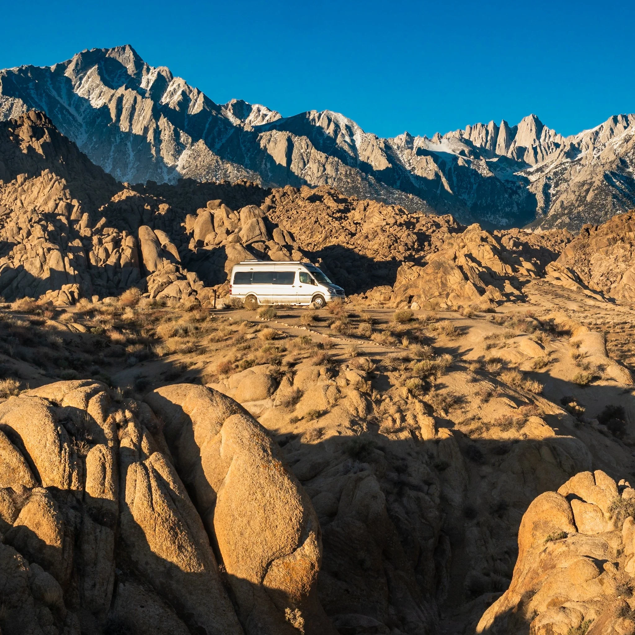My Sprinter camper van parked on rocky terrain at Alabama Hills with Mount Whitney in the background under a clear blue sky.