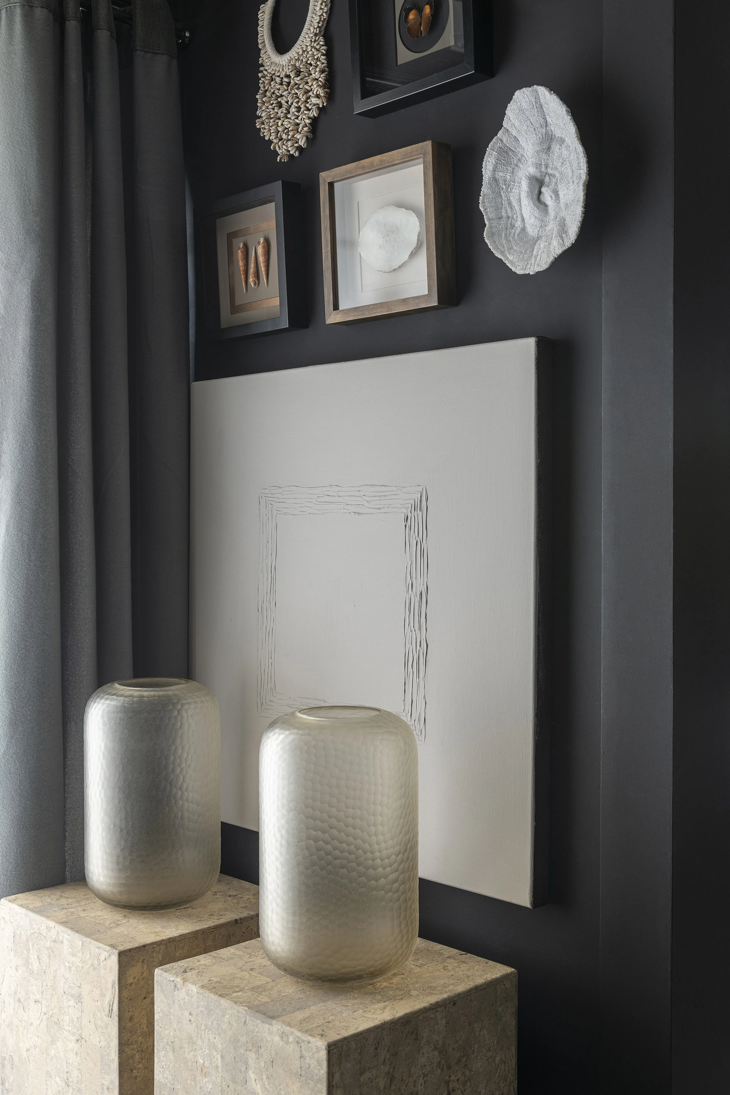 An image off 2 columns with a glass hurricane on top in front of a wall with some art and frames filled with unique decoration items.