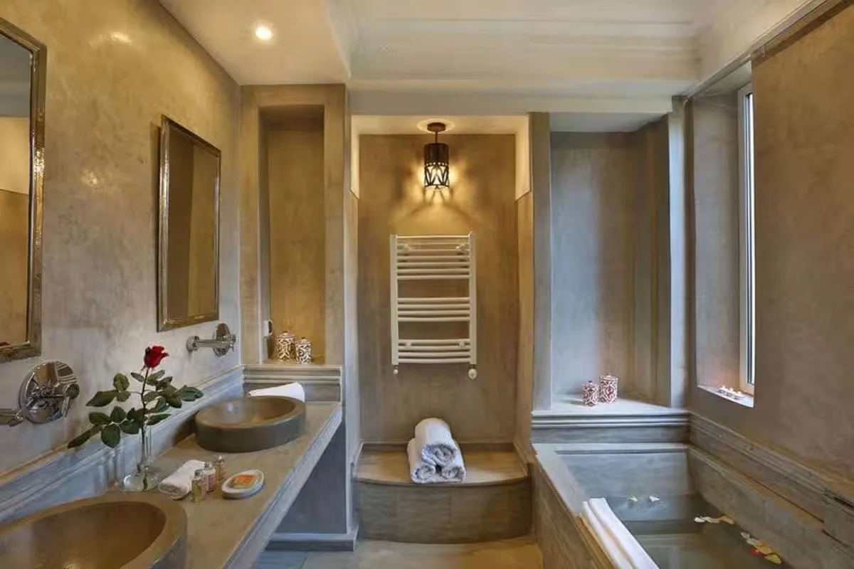 Salle de bain élégante avec deux lavabos, un bain moussant, miroirs, serviettes blanches, et décoration chaude et sophistiquée.Retraite pour femmes a marrakech au maroc