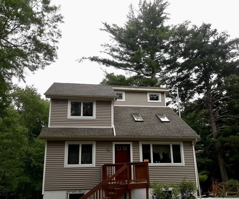 A three-story house with new beige siding, windows, and a new shingle roof in Lords Valley PA.