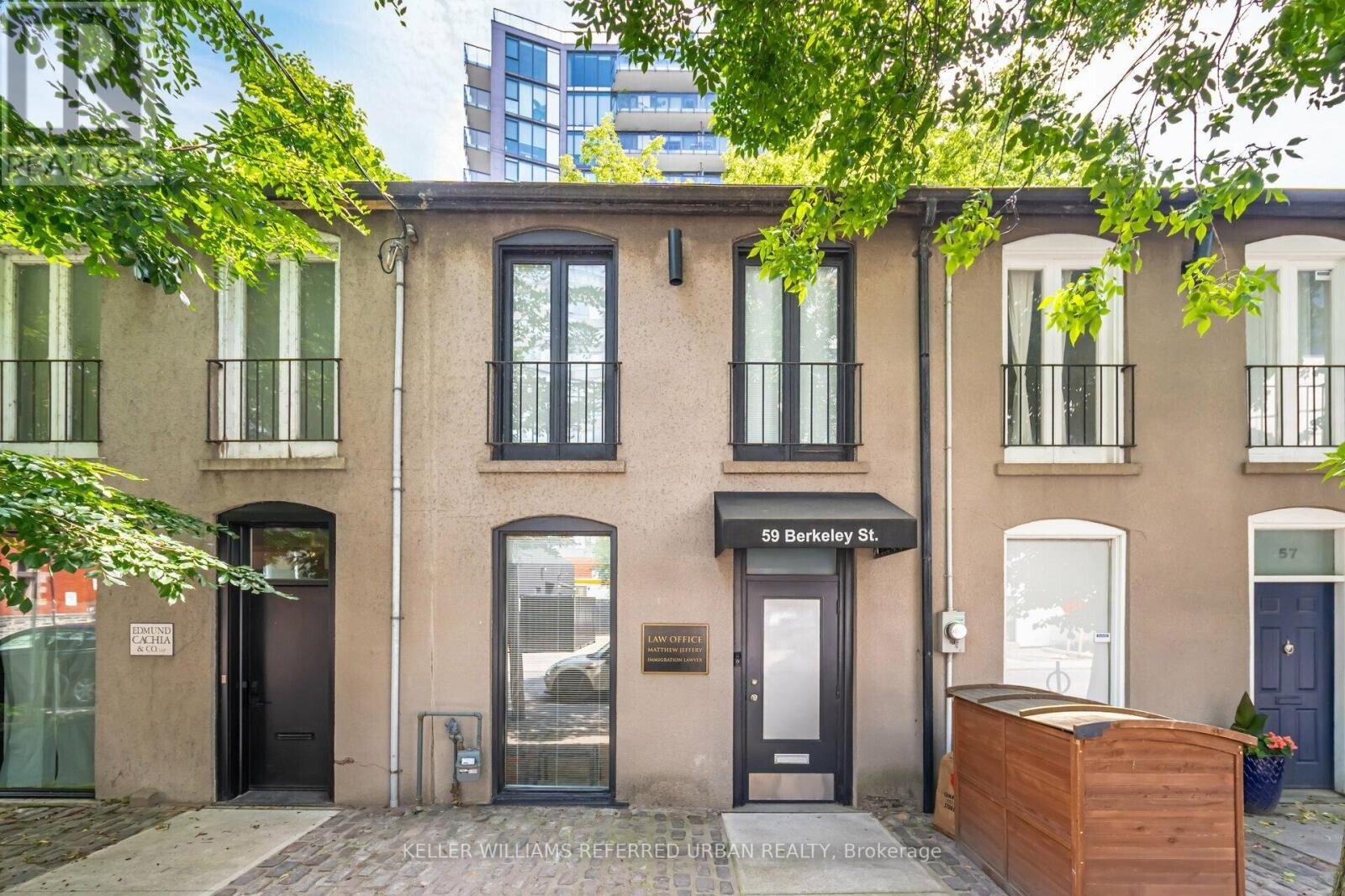 Street view of a law office located at 59 Berkeley St with modern exterior, large windows, awning, surrounded by greenery and neighboring buildings on either side.
