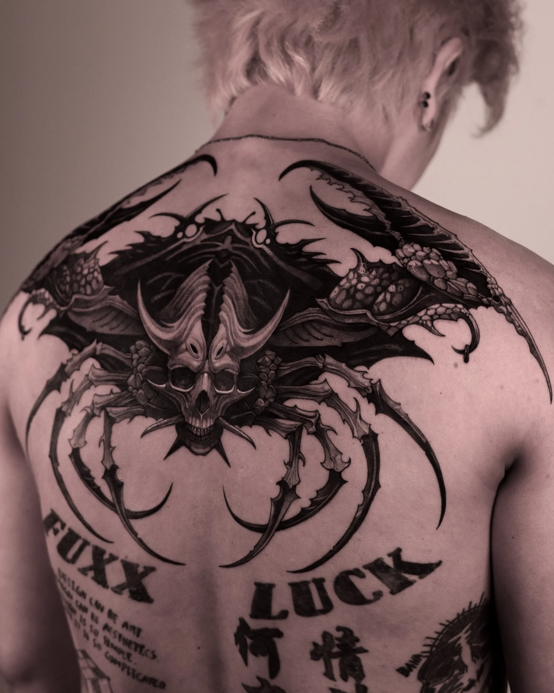 Man with large back tattoo featuring a detailed black ink design of a skull with horns and text on the shoulder blades. 47Volt Tattoo Artist | Hanok Studio | Toronto Tattoo Shop | Korean Artist | Blackwork Animal Tattoos