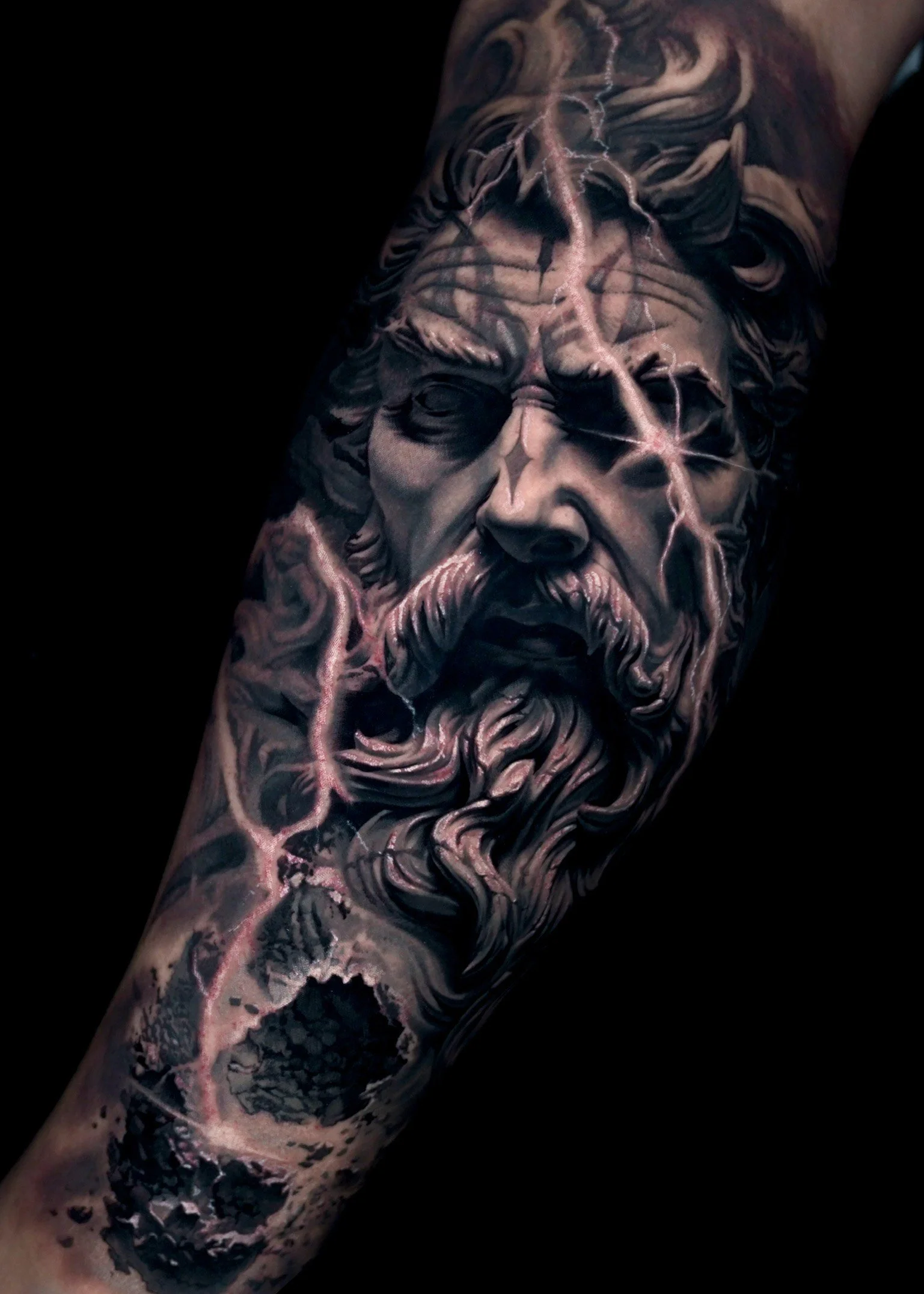 Realistic tattoo of a bearded man with lightning, resembling a mythological figure, on a forearm.