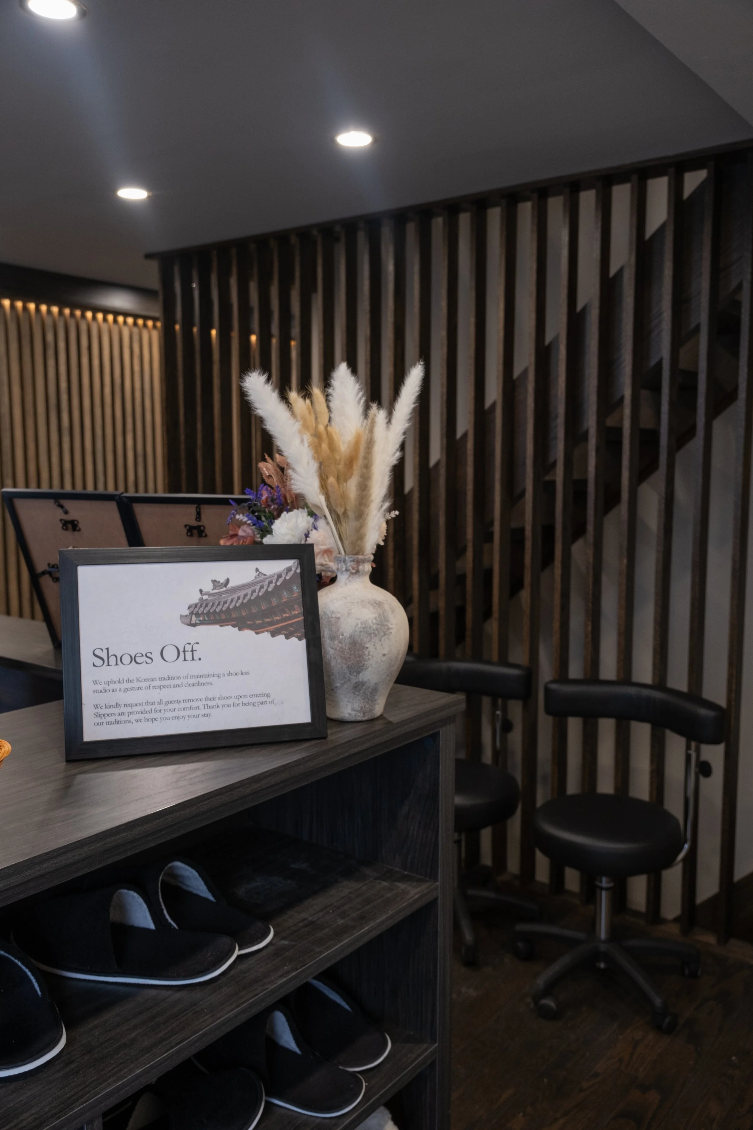 Reception area with "Shoes Off" sign, flower vase, and slippers on shelf