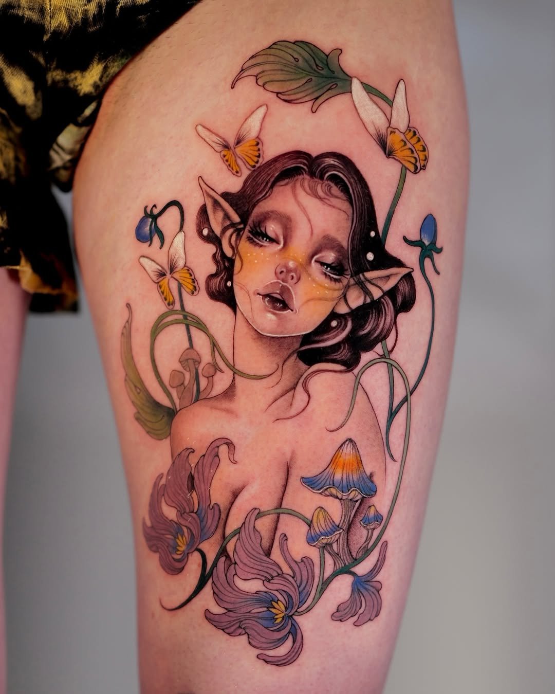 Tattoo of a fairy-like woman with elf ears, surrounded by flowers and butterflies, with detailed shading and vibrant colors by Roha
