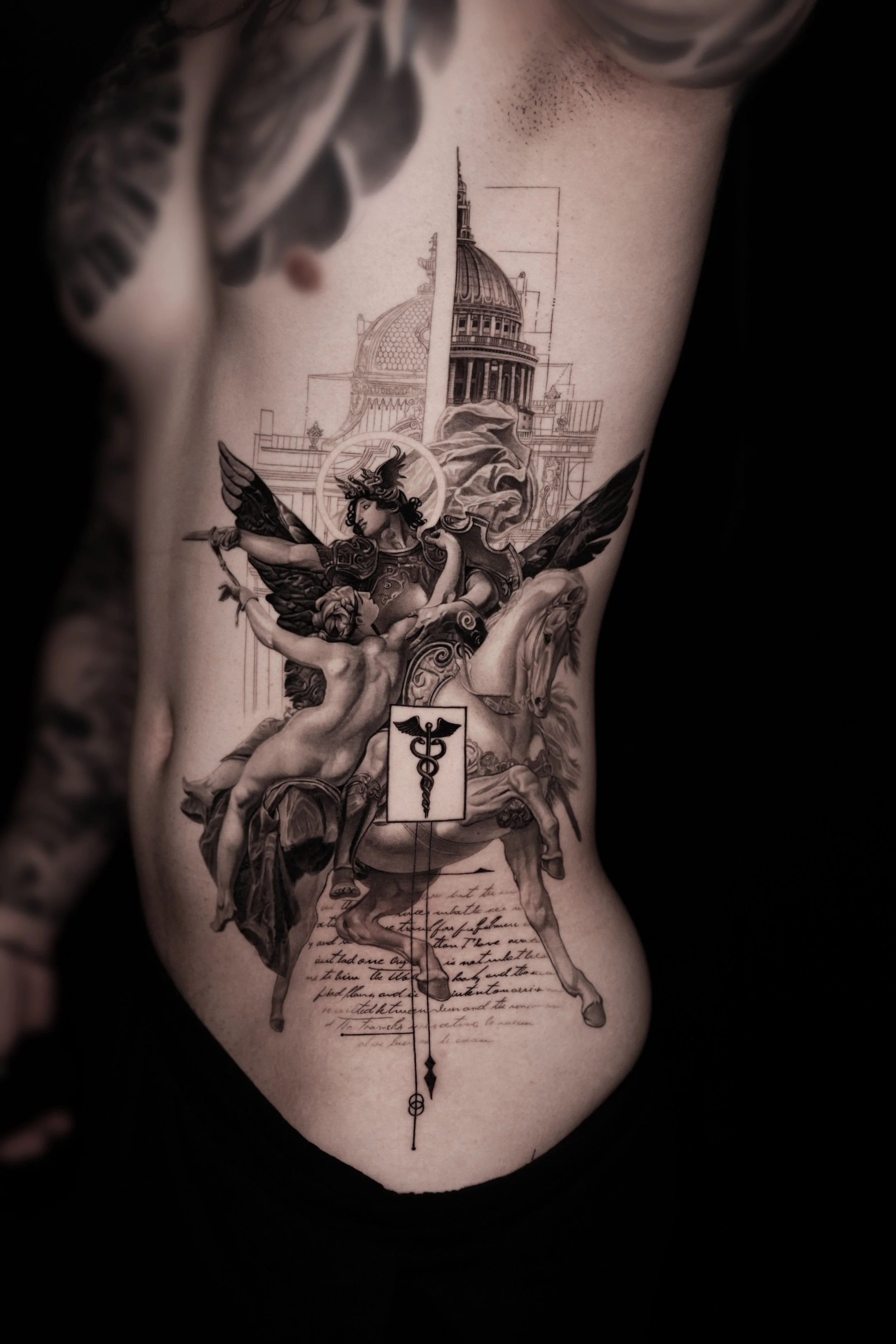 Detailed black and gray tattoo on a person's side, featuring a mythological scene with winged figures, horses, a cityscape with domed buildings, and handwritten script.