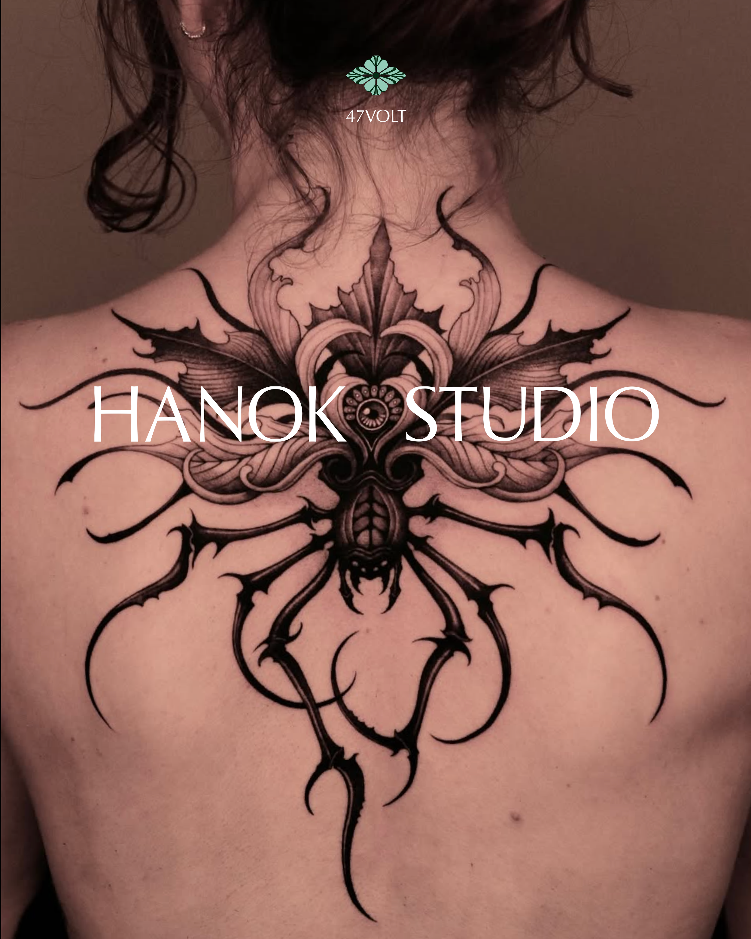 Back of a person with an intricate black tattoo of a spider, wings, and floral designs covering the upper back and nape of the neck.