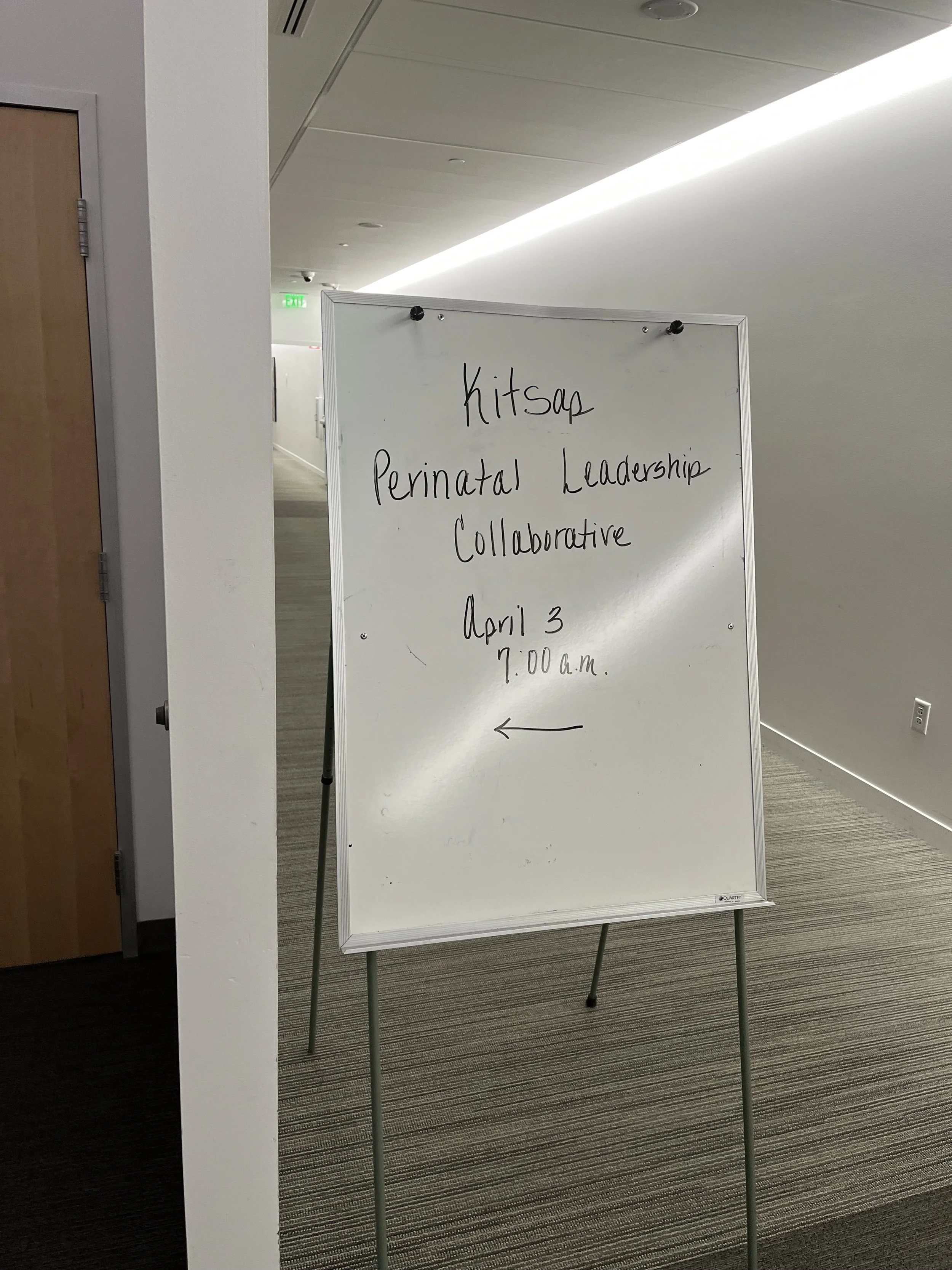 Whiteboard with handwritten text announcing a Kitsap Perinatal Leadership Collaborative meeting on April 3rd at 7:00 a.m., with an arrow pointing to the left.