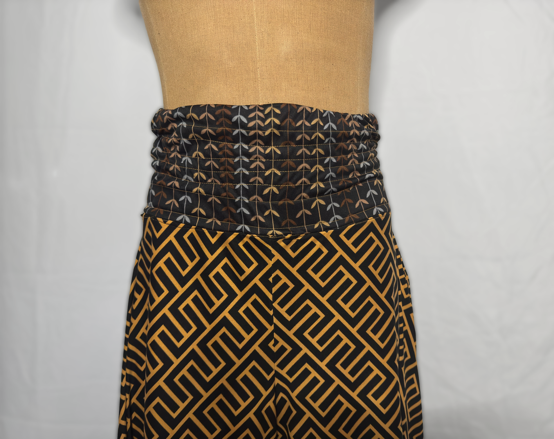 Close-up of a mannequin wearing a wrapped black skirt with gold and white leaf pattern on the waistband and a black and gold geometric pattern on the skirt.
