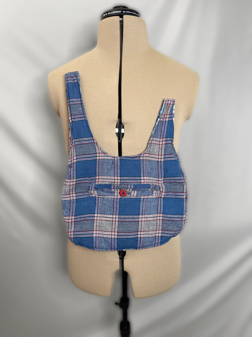 A torso mannequin wearing a plaid backpack with blue, red, and white patterns.
