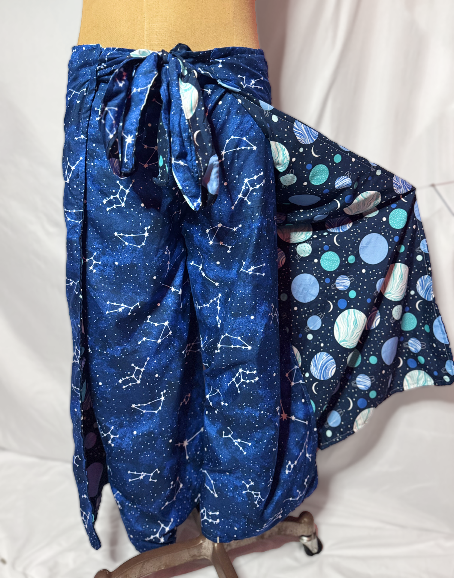 Pair of navy blue pajama pants with star constellations and galaxy patterns hanging on a mannequin.