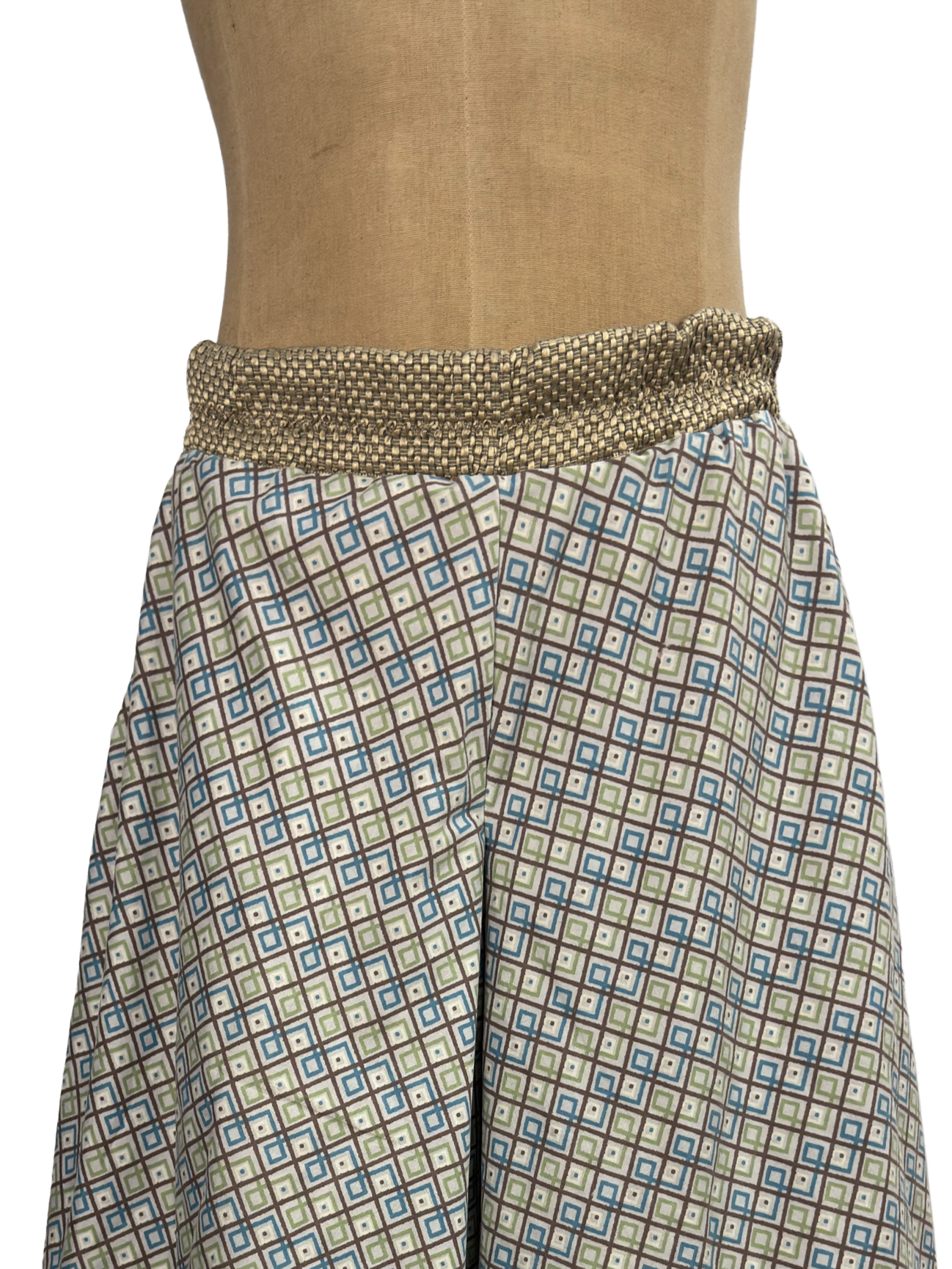 Close-up of a mannequin wearing a wrapped black skirt with gold and white leaf pattern on the waistband and a black and gold geometric pattern on the skirt.