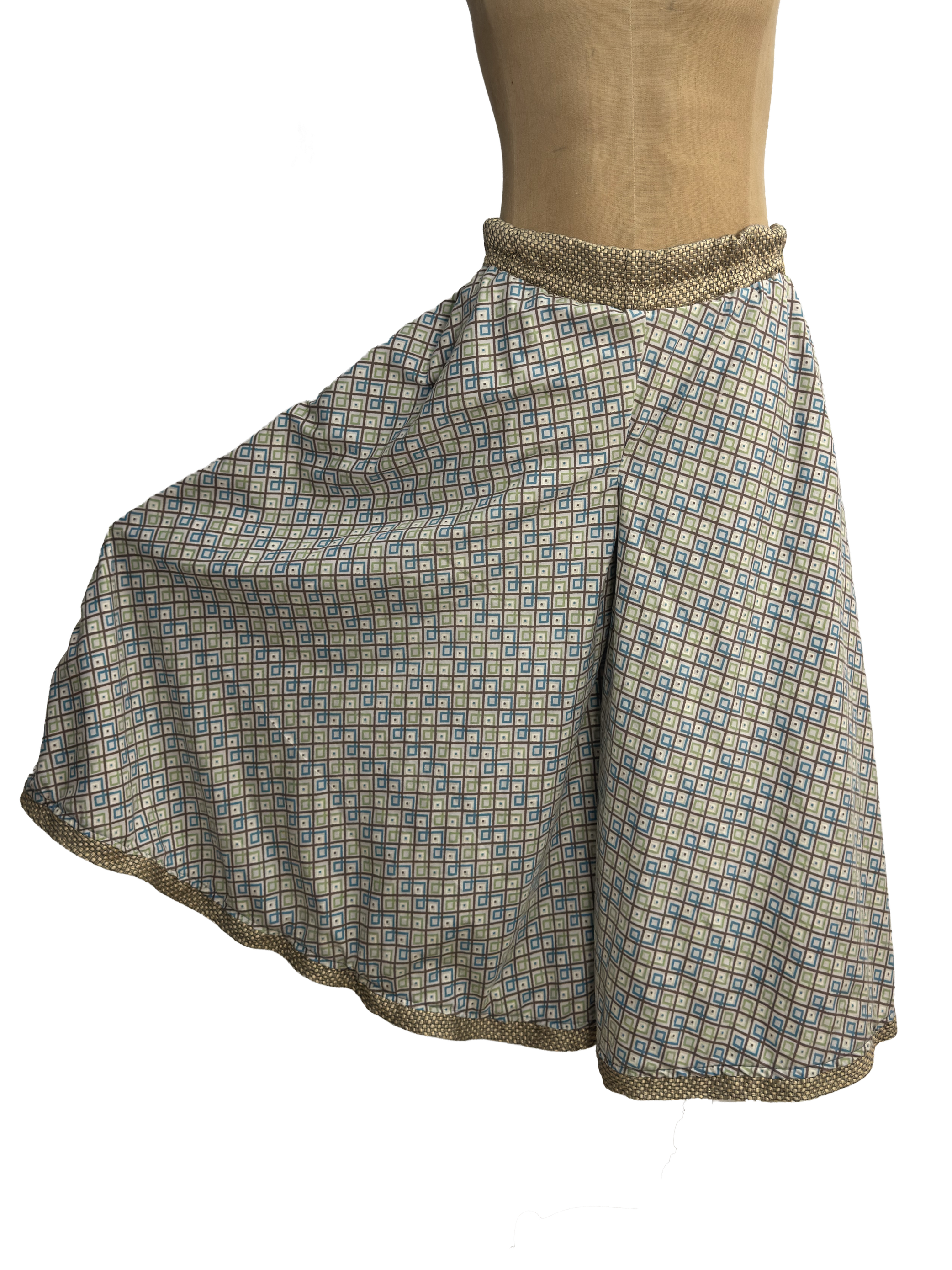 Wide-leg palazzo pants with one leg flared, in a blue and tan geometric square print with a matching dotted elastic waistband and hem trim, shown on a dress form