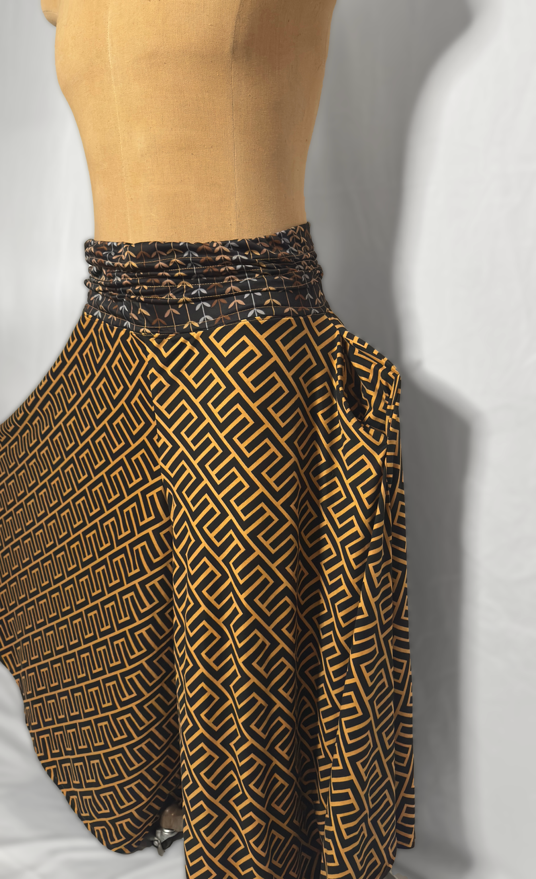 Close-up of a mannequin wearing a patterned skirt with a black and orange geometric design and a matching waist tie.