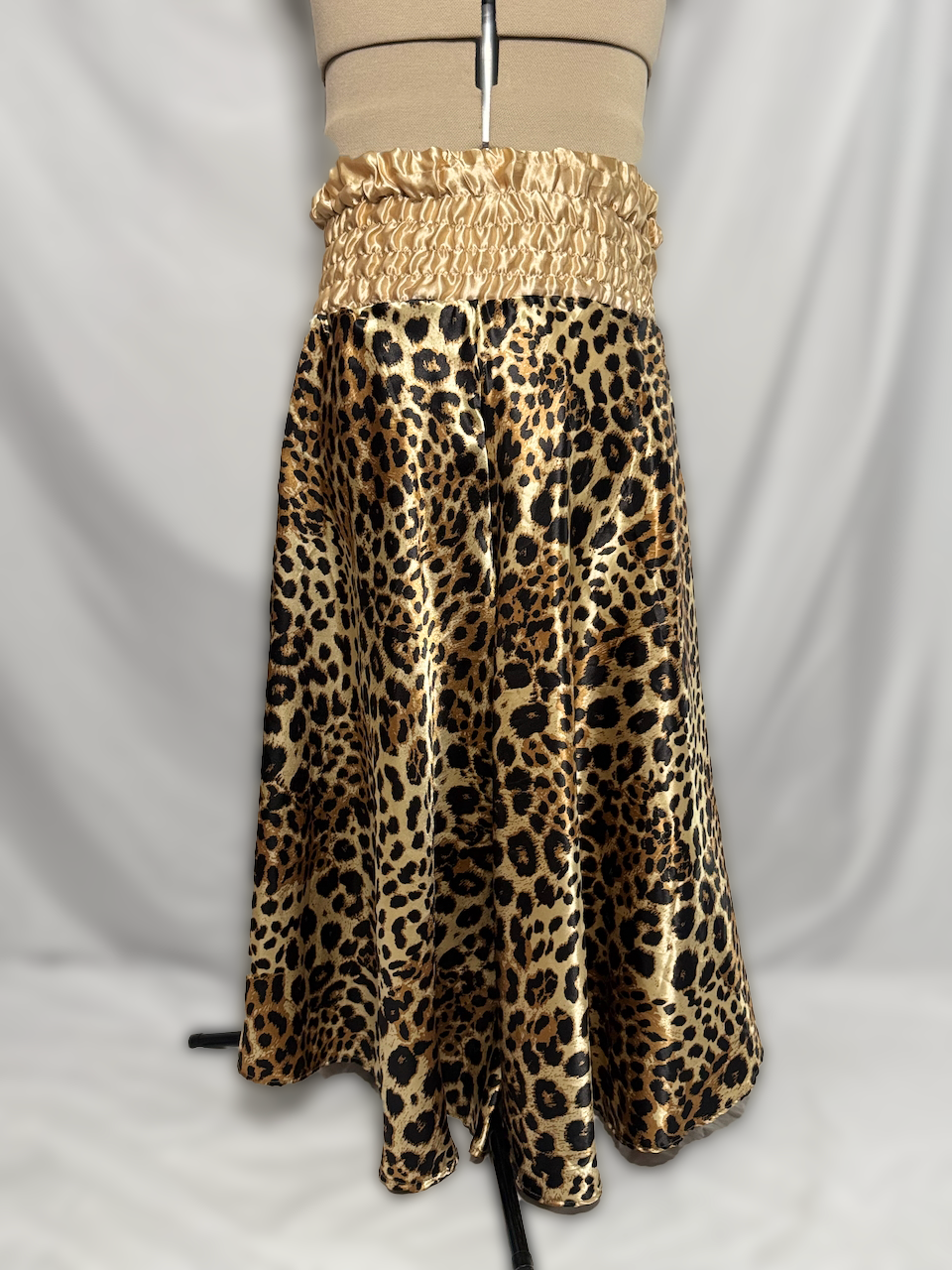 A leopard print skirt with a wide golden satin waistband displayed on a mannequin against a white background.