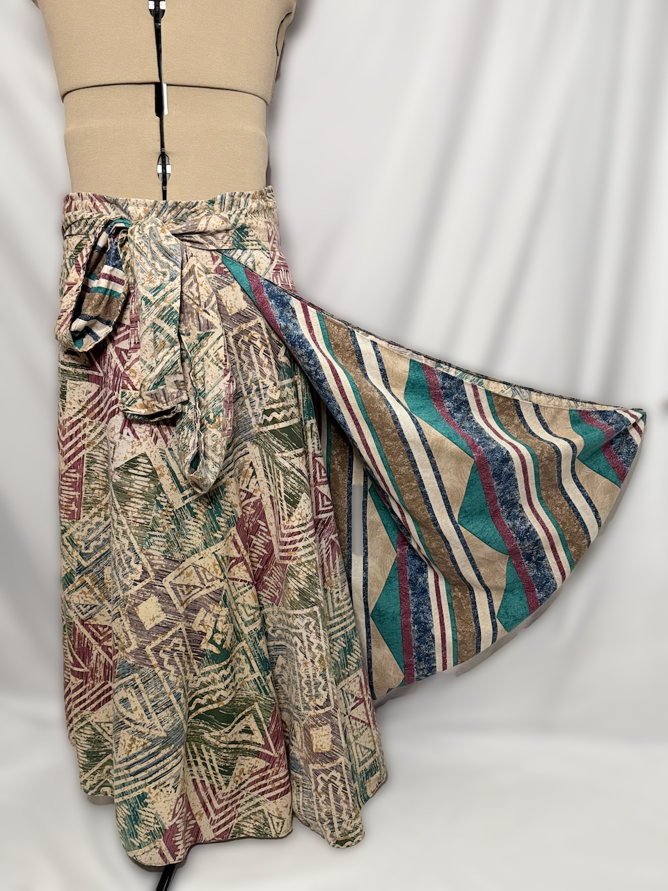 Mannequin dressed in a beige fitted top and a long, patterned skirt with a tied waist and a contrasting geometric patterned fabric on the side.
