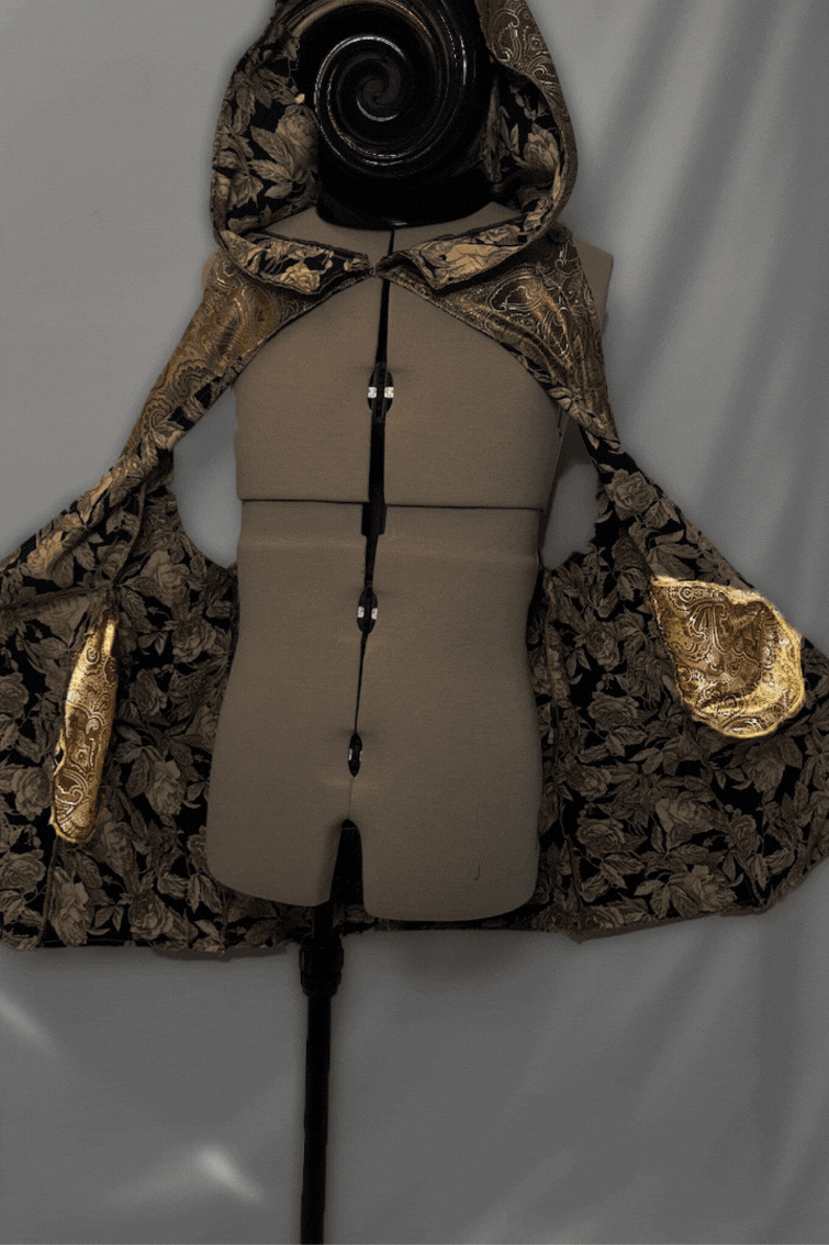 A dress form mannequin wearing a black and gold embroidered cape with a floral pattern and a hood, displayed against a plain background.