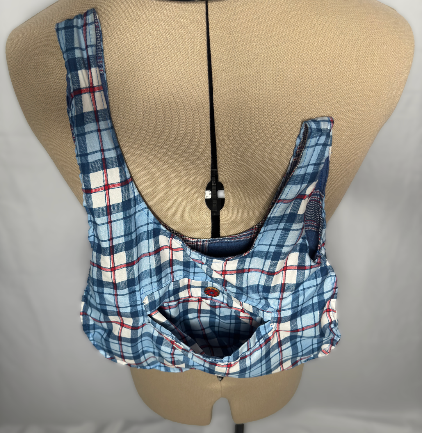 A plaid shirt with blue, white, and red checks draped over a beige mannequin torso, partially unbuttoned with the front pocket visible.