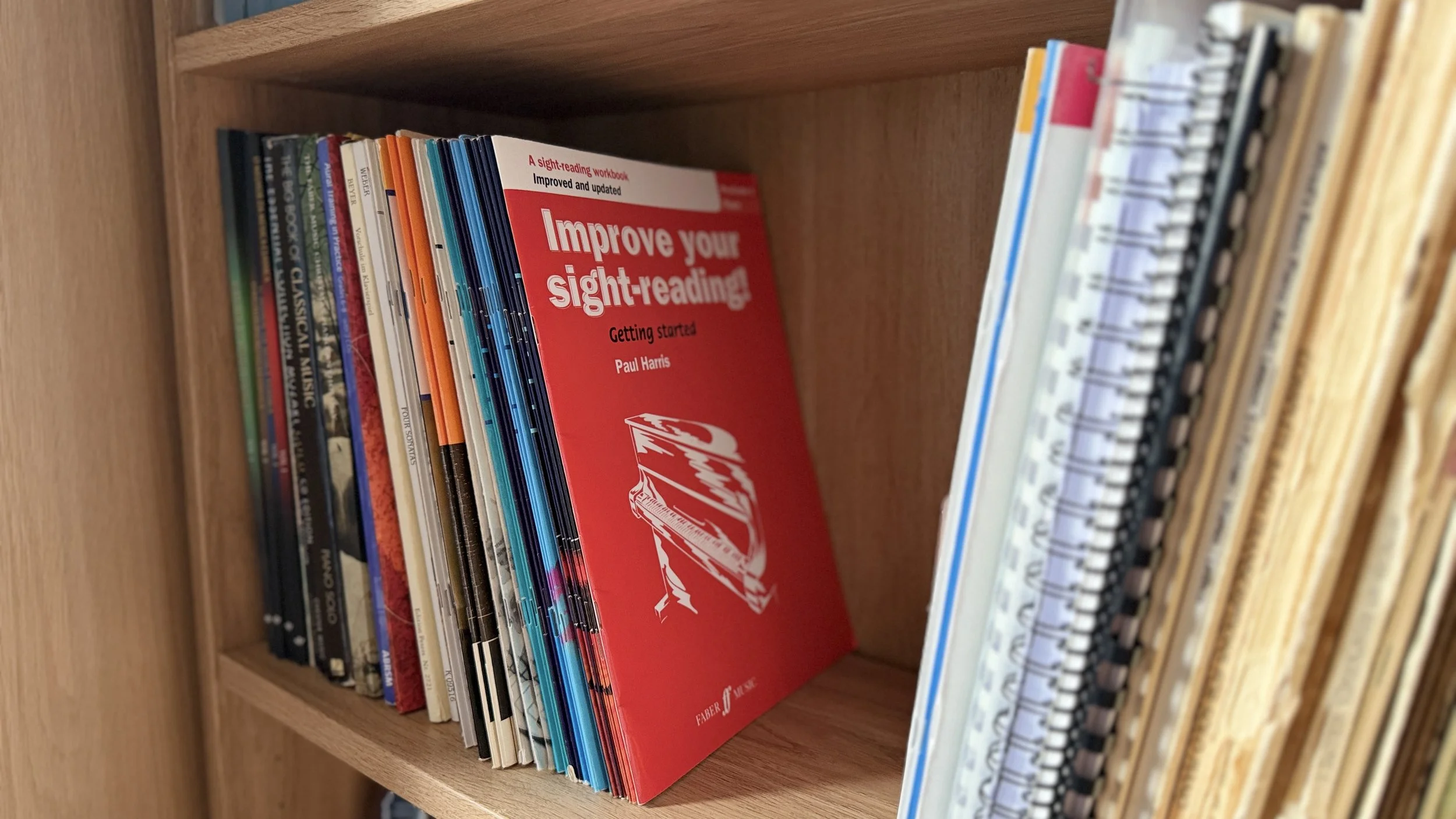 A bookshelf holding various books with a red book titled 'Improve your sight-reading!' by Paul Harris visible.