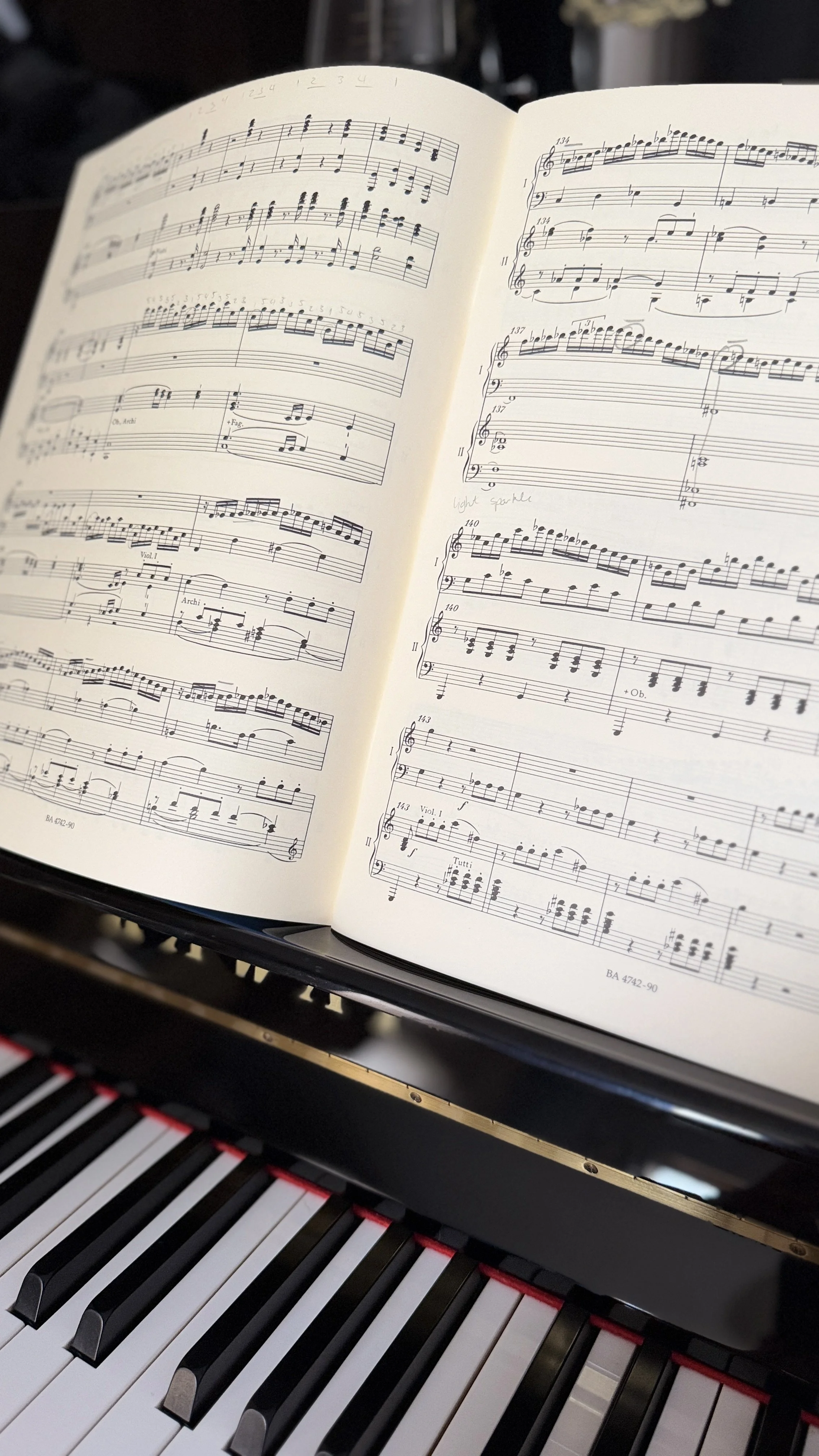 Open sheet music book placed on a Kawai upright piano, showing an annotated copy of Mozart Piano Concerto No.25 in C major.