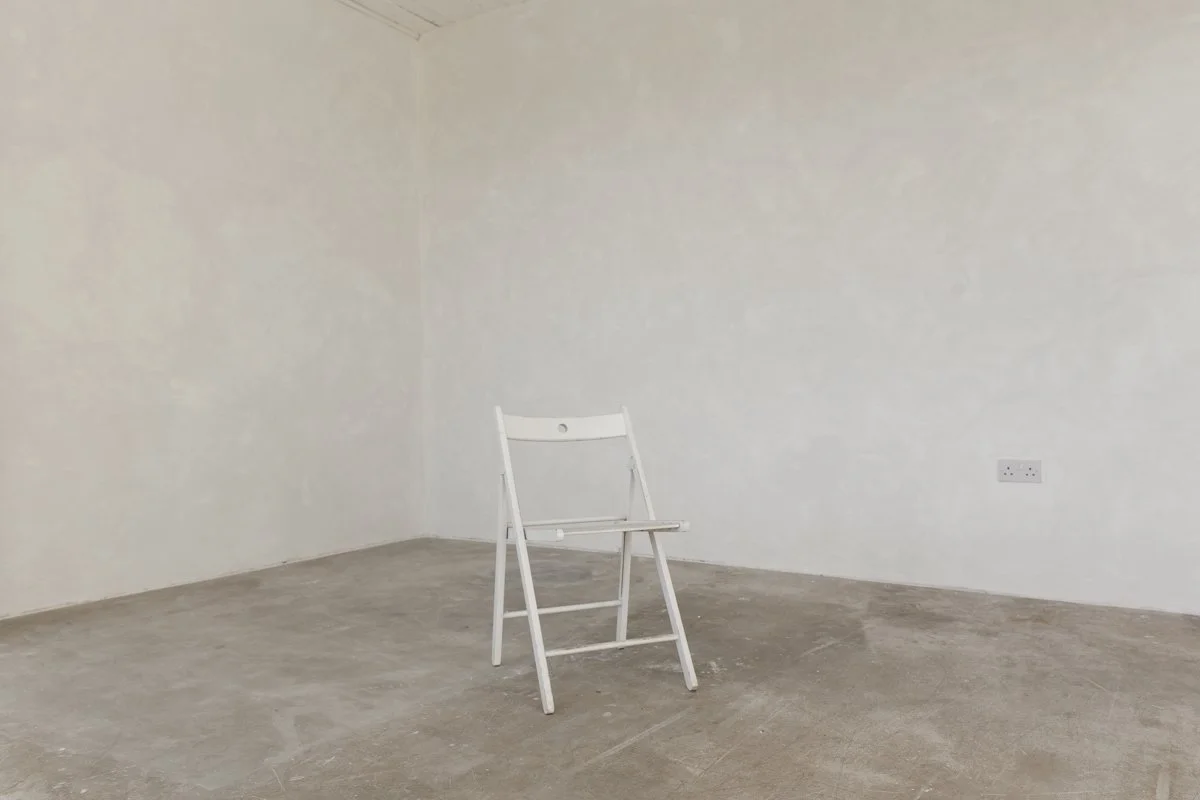 Empty room with white walls, concrete floor, and a single white folding chair.