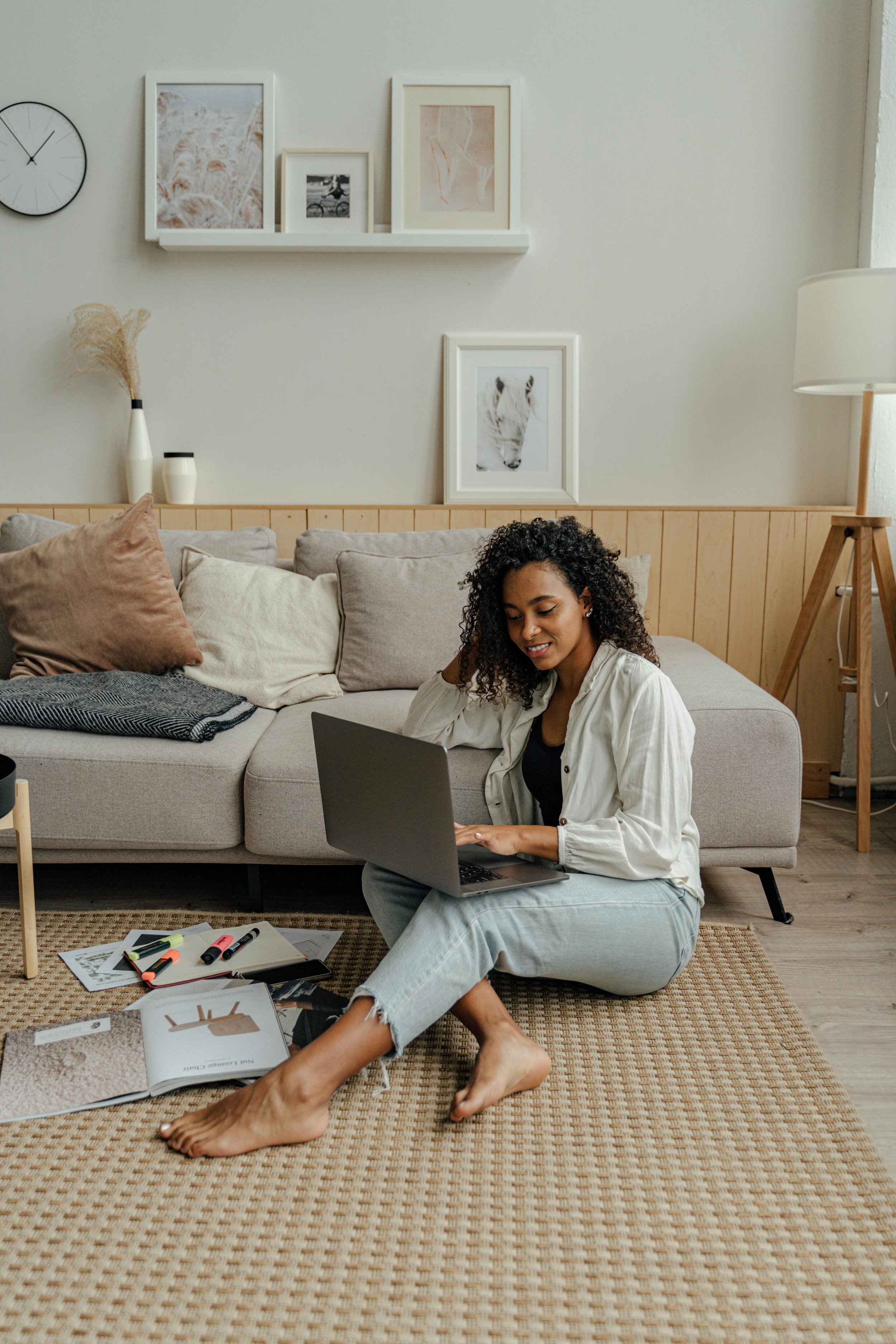 Woman sitting on floor in front of couch with laptop in her lap, representing virtual therapy groups and community-based healing.