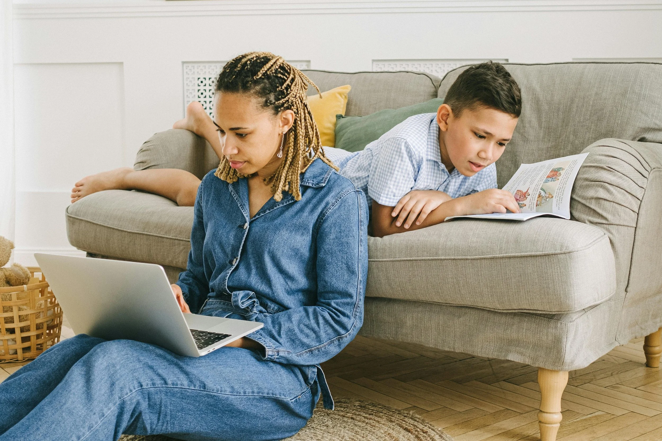 Mother working on a laptop while her child does homework nearby, reflecting the coexistence of connection, distance, and responsibility in family relationships.